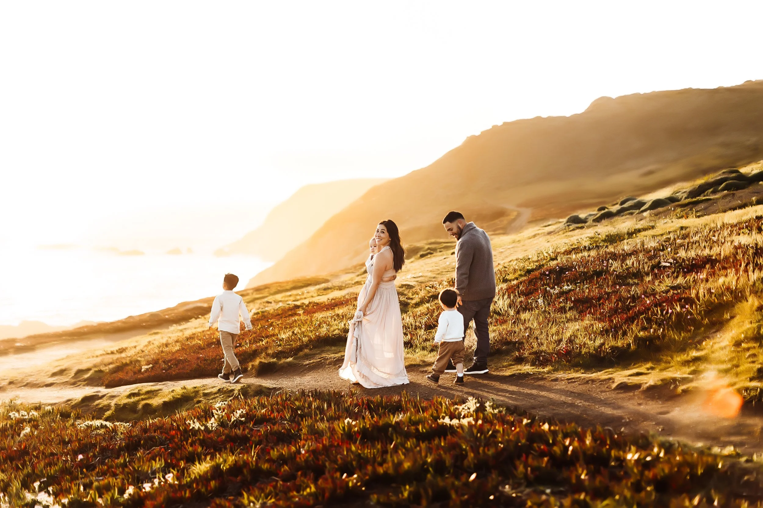 A family of five enjoying a walk along a shoreline during sunset, with mountains in the background.