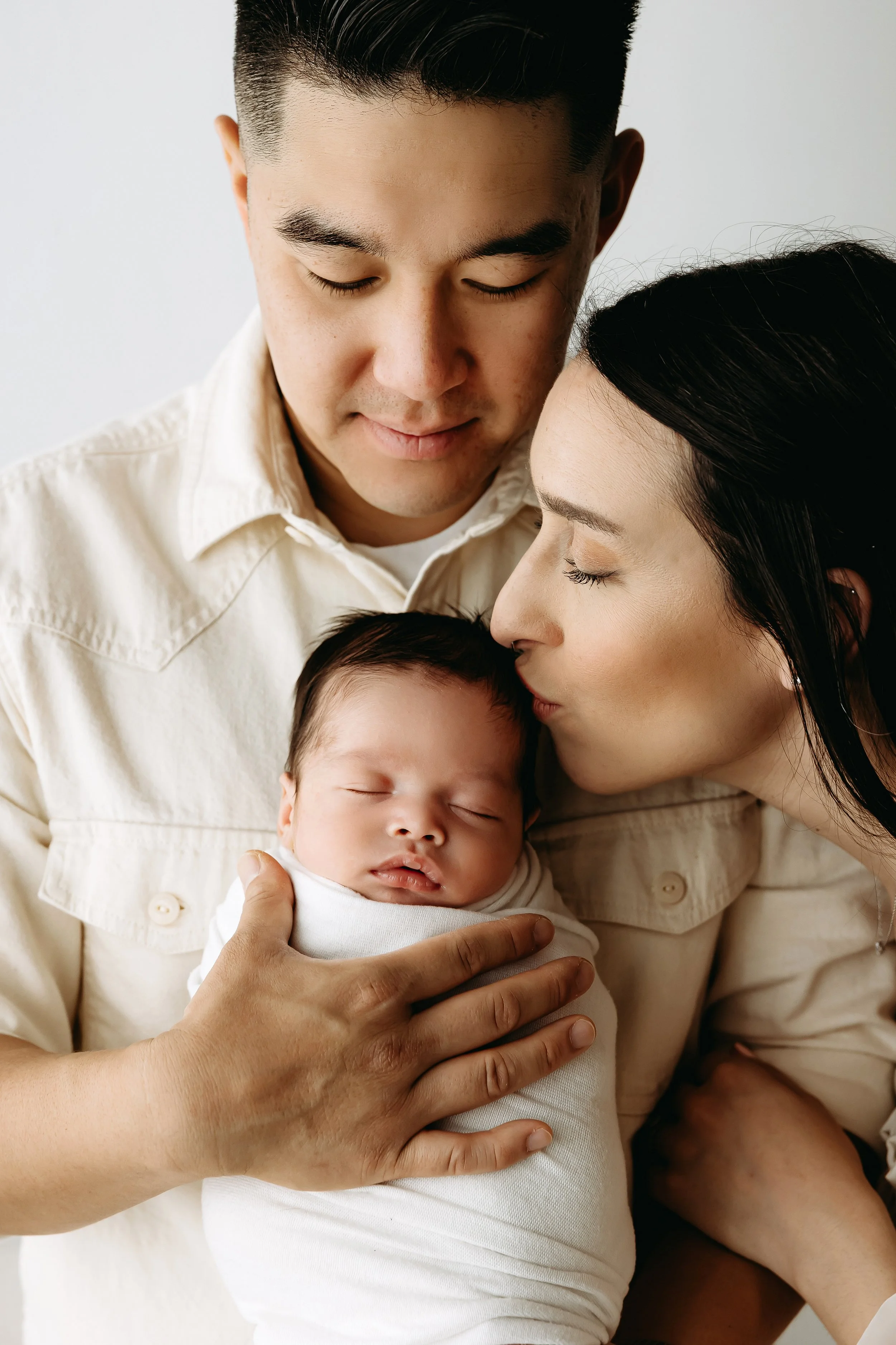 A family of four, including a man, woman, and two babies, is close together with their eyes closed, showing a moment of intimacy and affection.