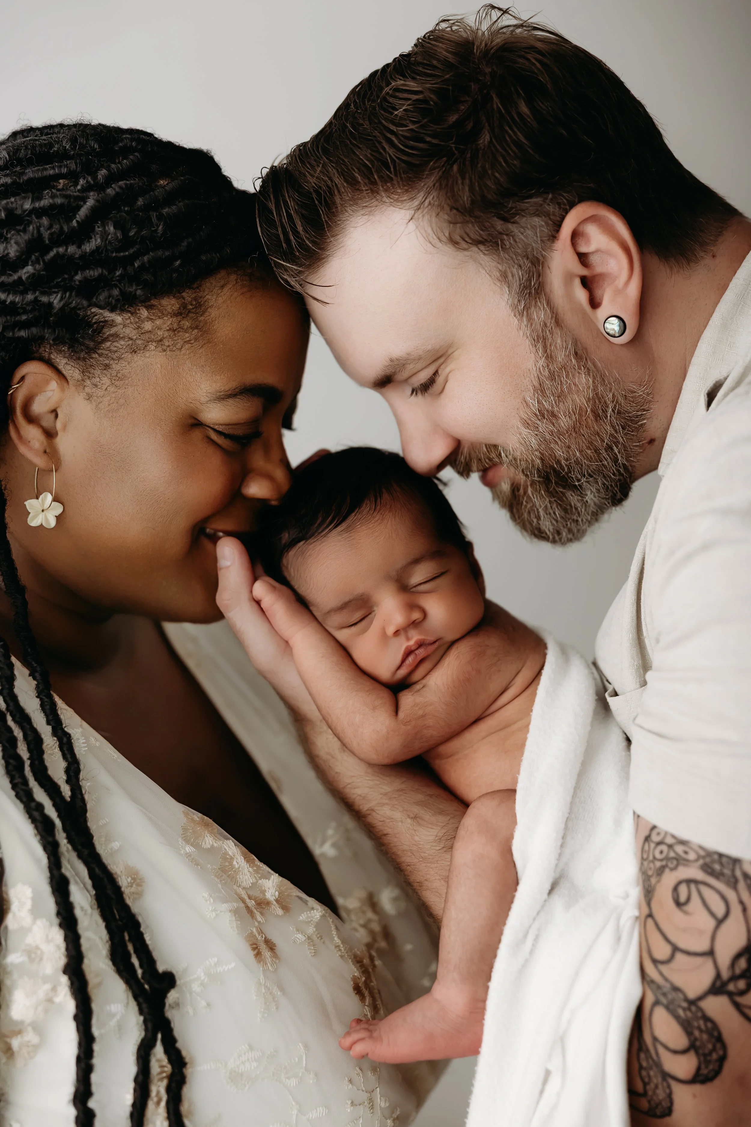 A close-up of a diverse couple holding their newborn baby, with their foreheads touching and eyes closed, in a tender moment.