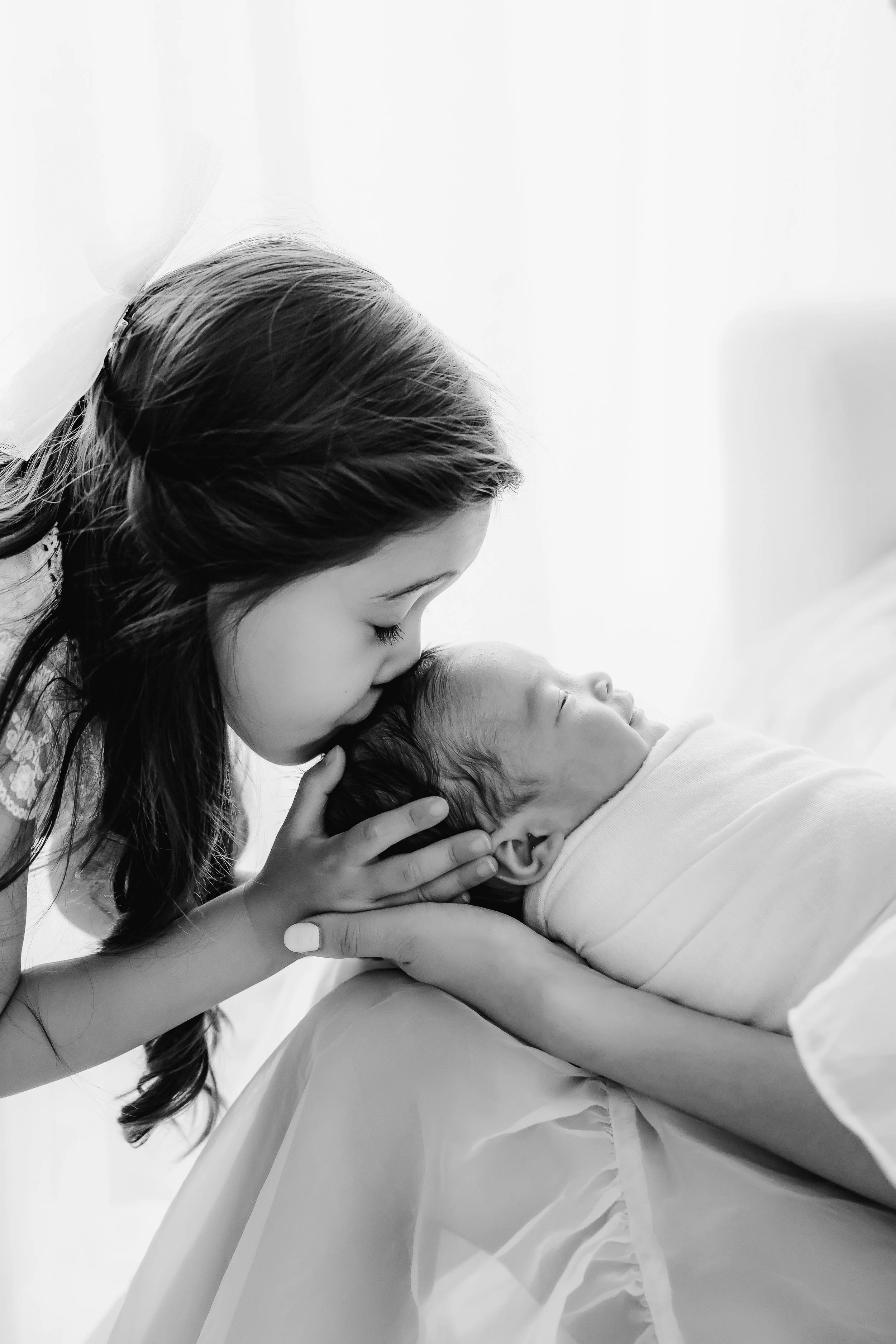 A woman gently kisses a newborn baby on the forehead while holding the baby's head, both lying down on a bed. The scene is tender and intimate, with soft lighting and a calm, loving atmosphere.