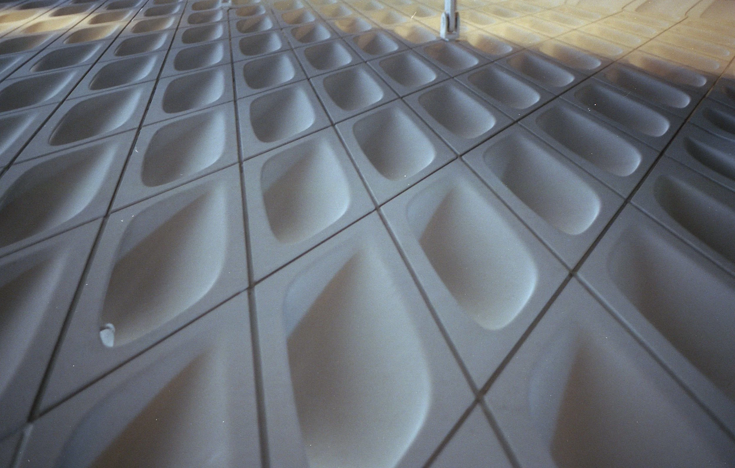 A floor with multiple gray, square-shaped tiles featuring indentations or moldings in the center of each tile, creating a pattern on the surface.