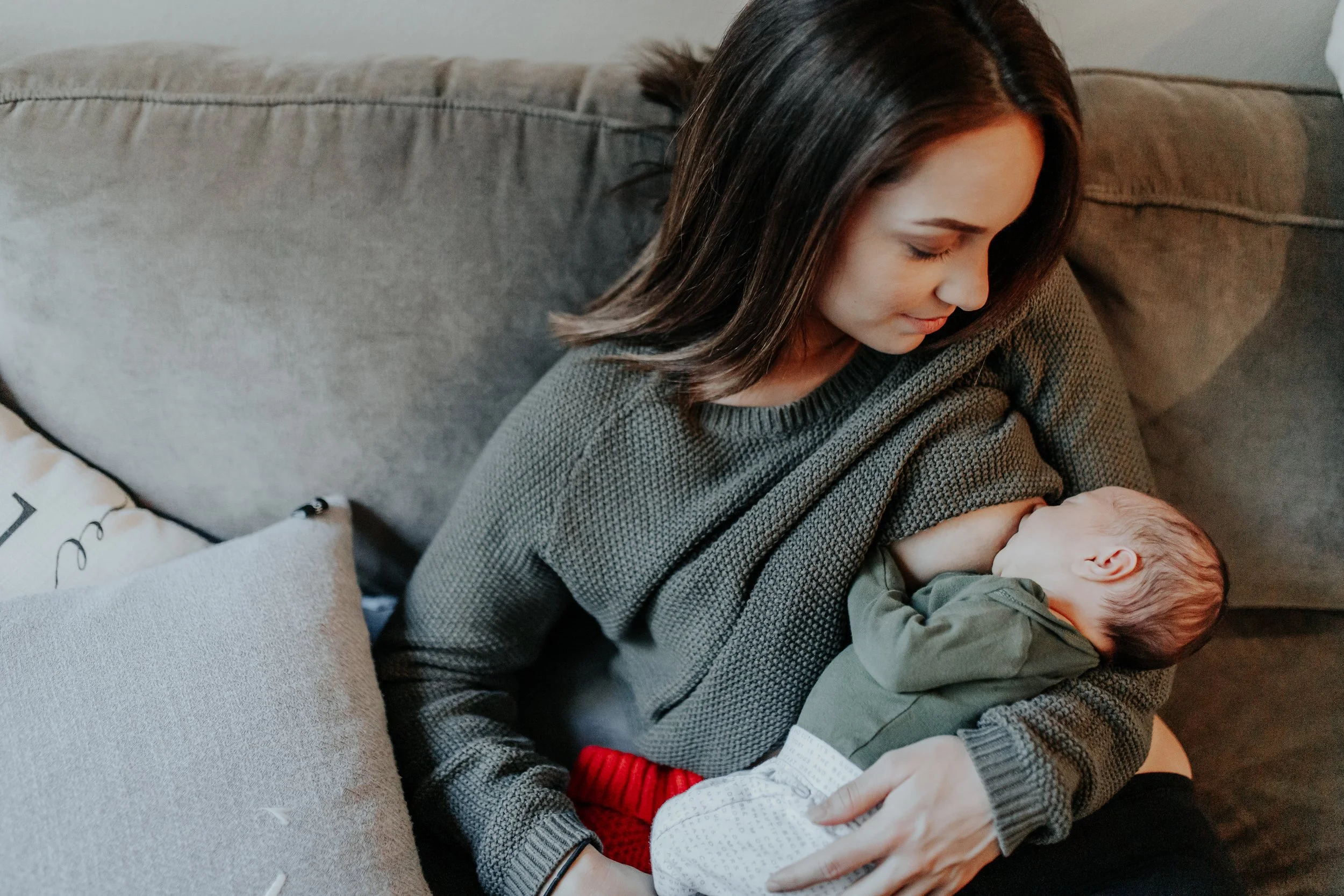 Woman sitting on couch breastfeeding newborn
