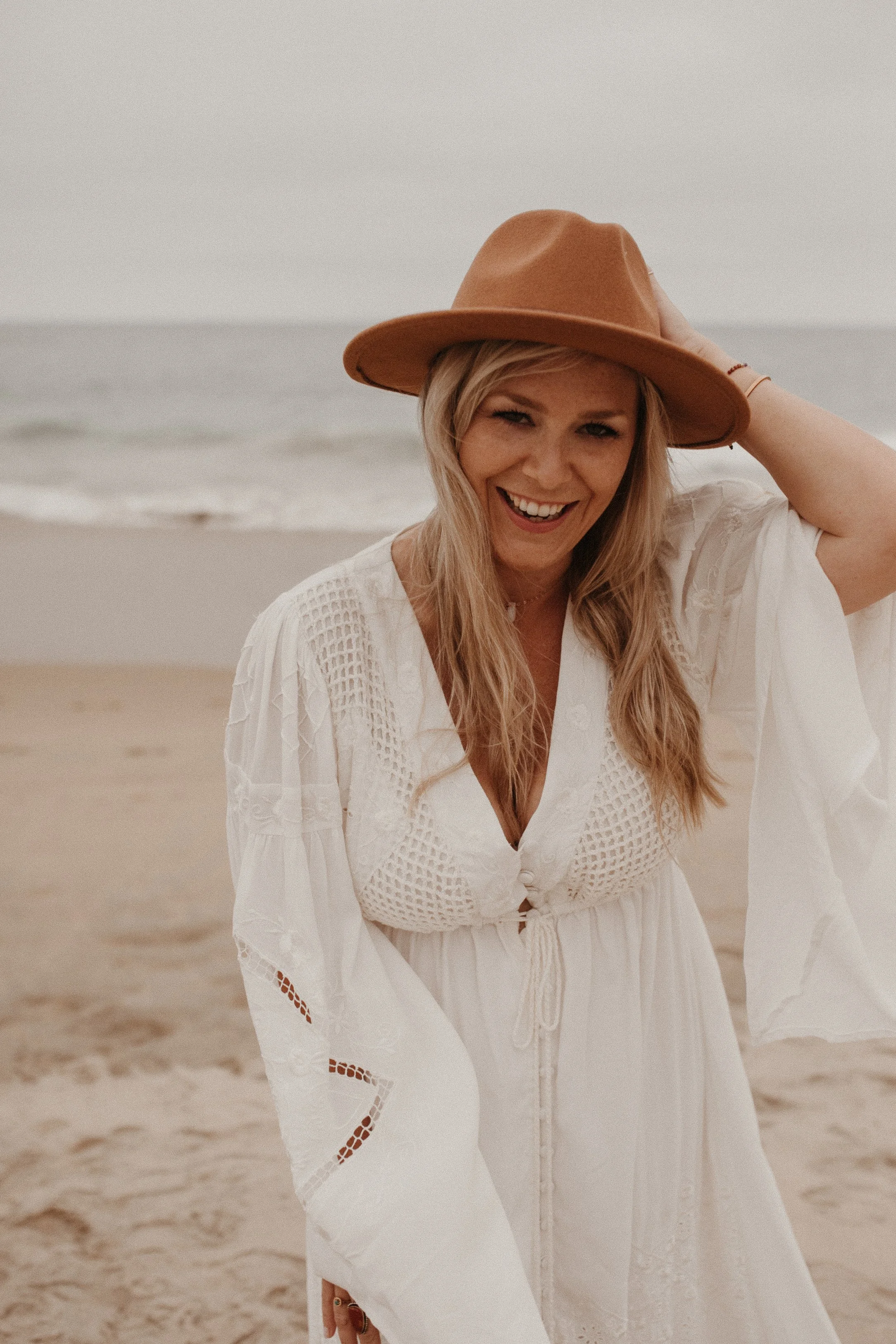 Woman in white dress and brown hat smiling on a beach