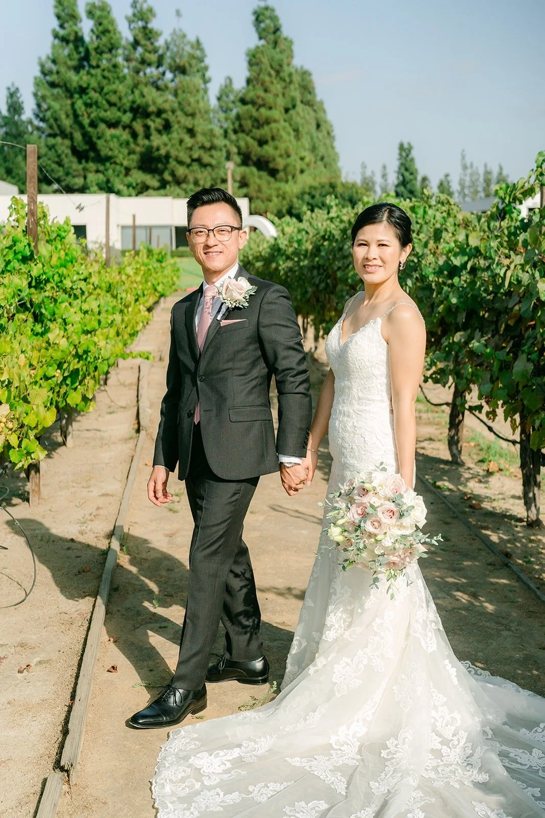 Alex and Xuemin walking hand in hand down a vineyard row