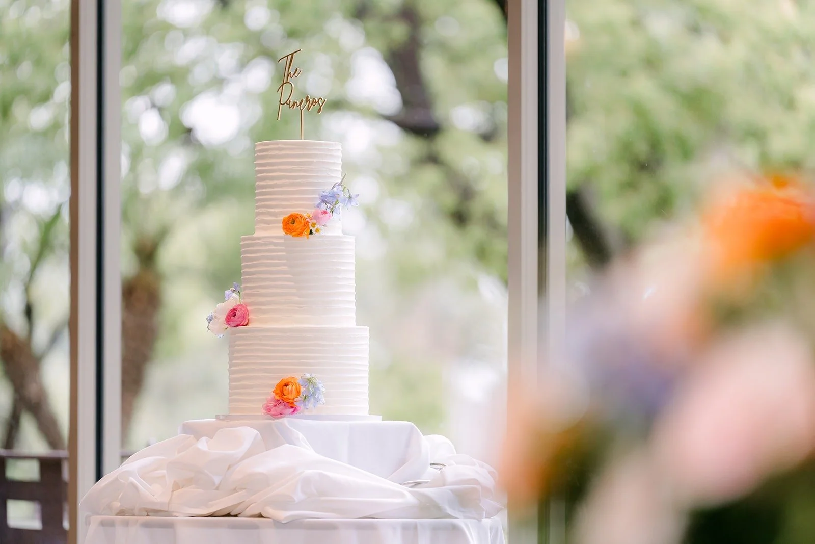 The three tier white wedding cake with pastel sugar flowers by the window