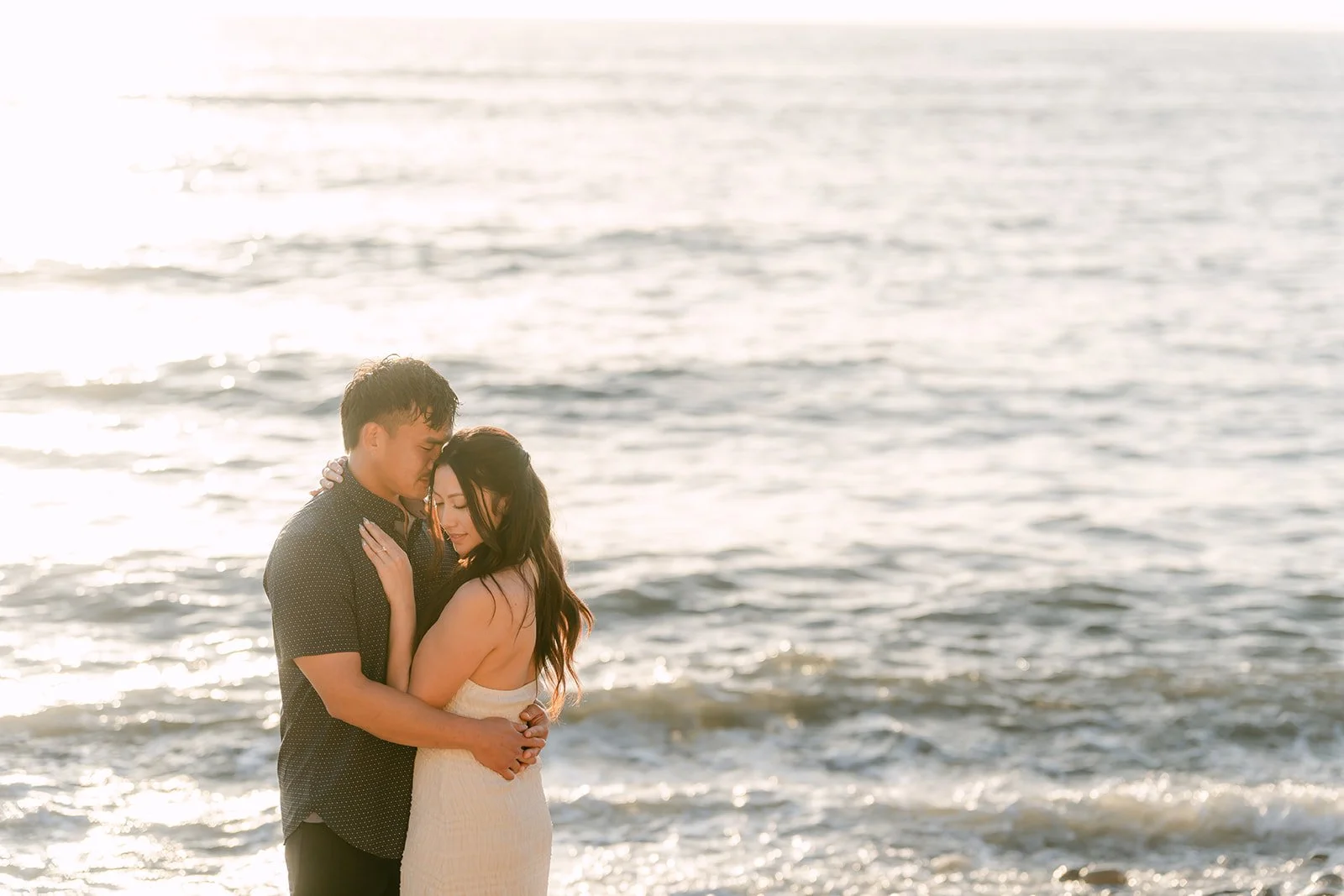 Victoria and Andrew touch foreheads as the sun lowers over the ocean.