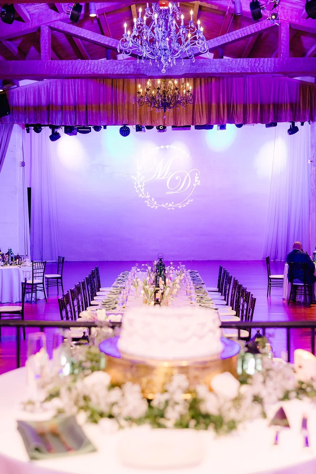 The heart shaped wedding cake under the chandelier in the ballroom