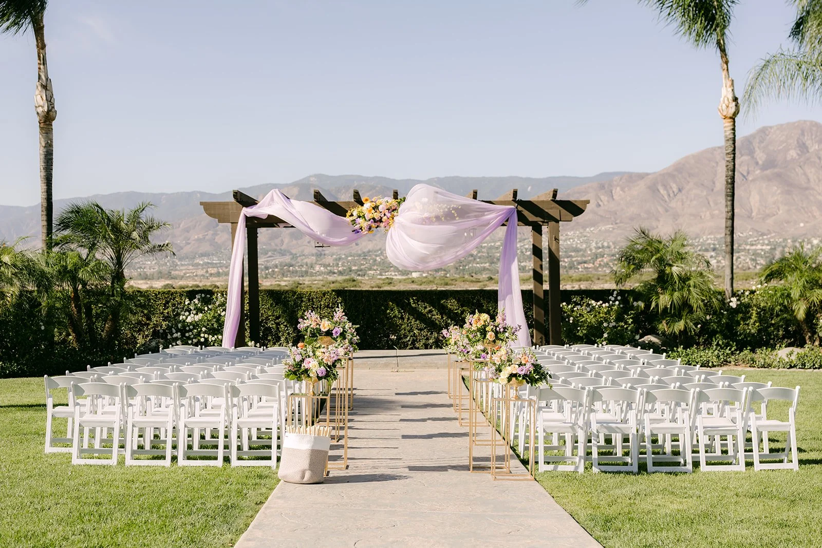 The ceremony site at The Grove of Redlands with white chairs, a draped arch and mountain views.