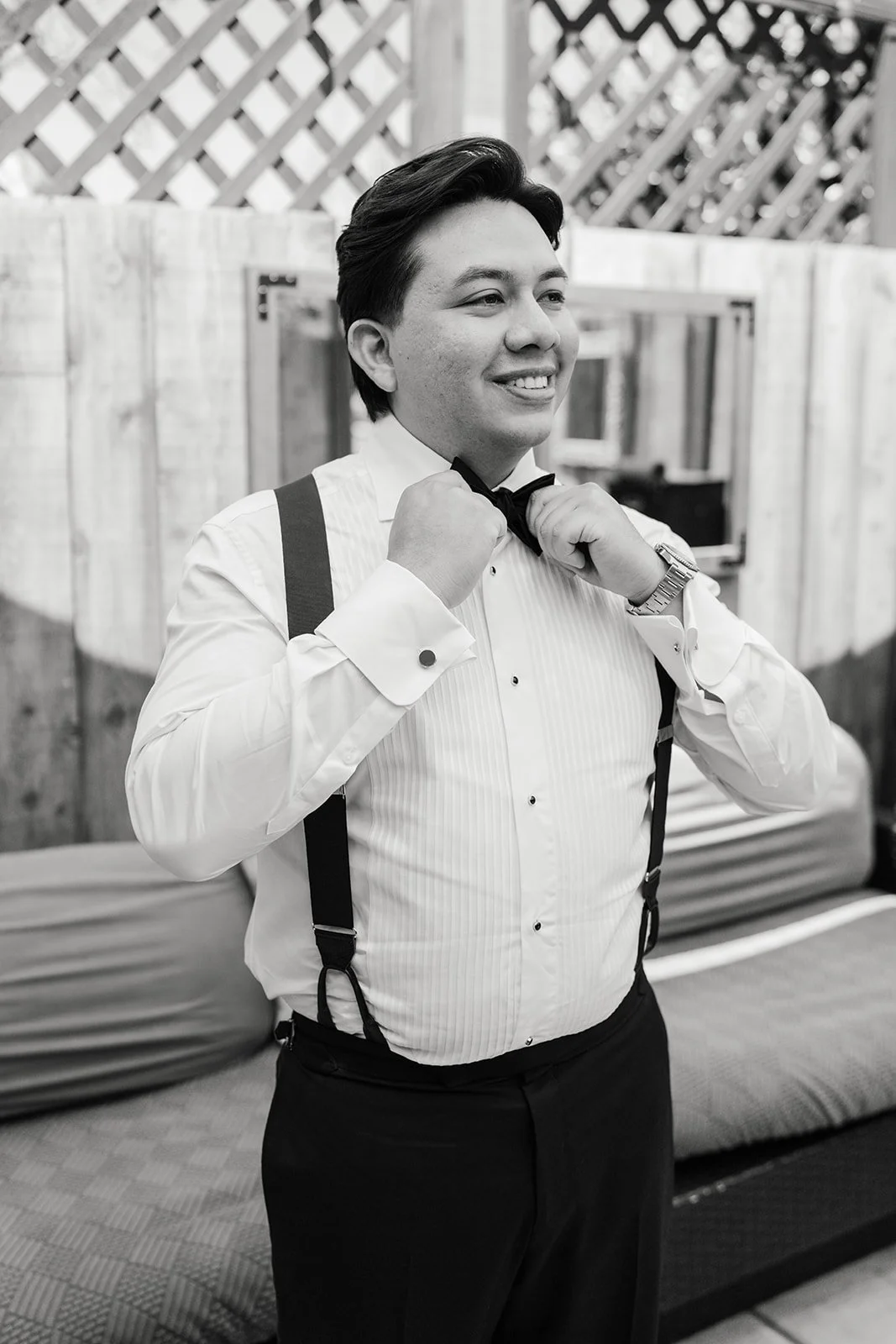 Black and white photo of the groom adjusting his bow tie