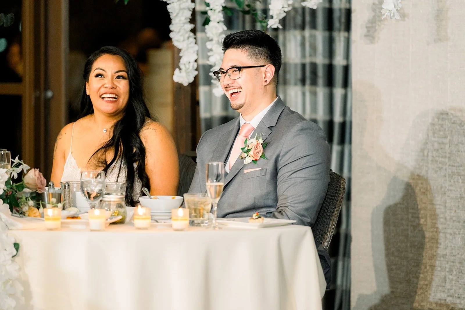 Betsy and Mikey smile at the speeches from the sweetheart table, photographed by One and Only Production