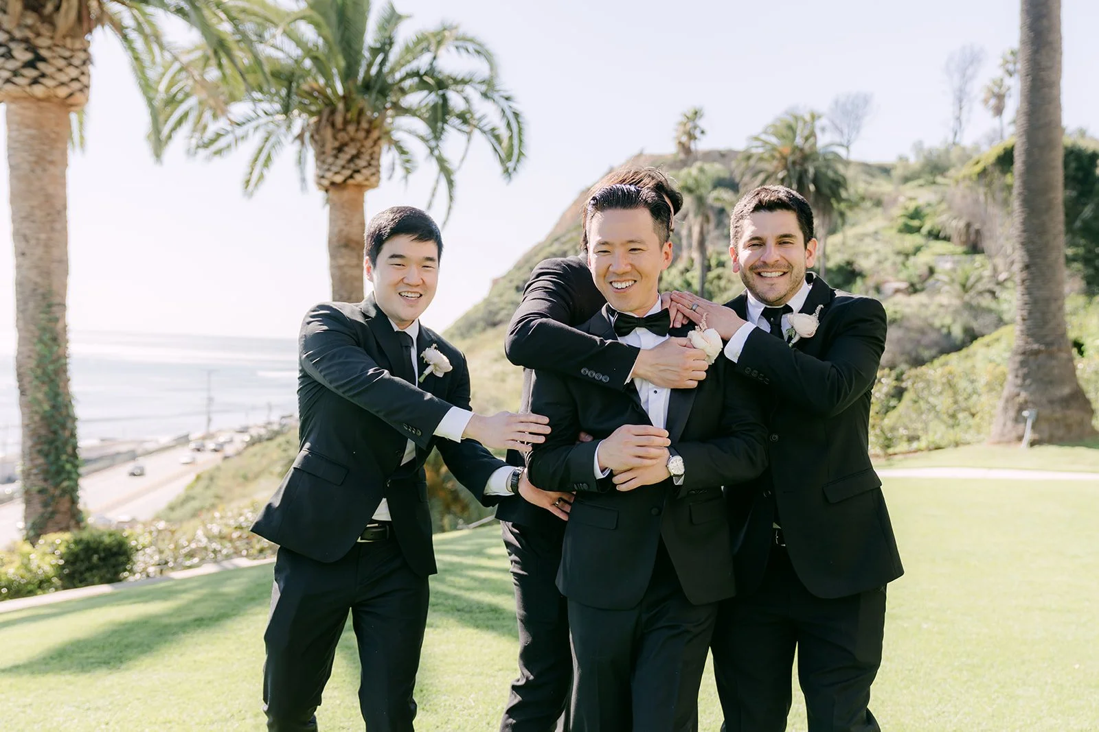 Groom and groomsmen hugging and laughing on the lawn