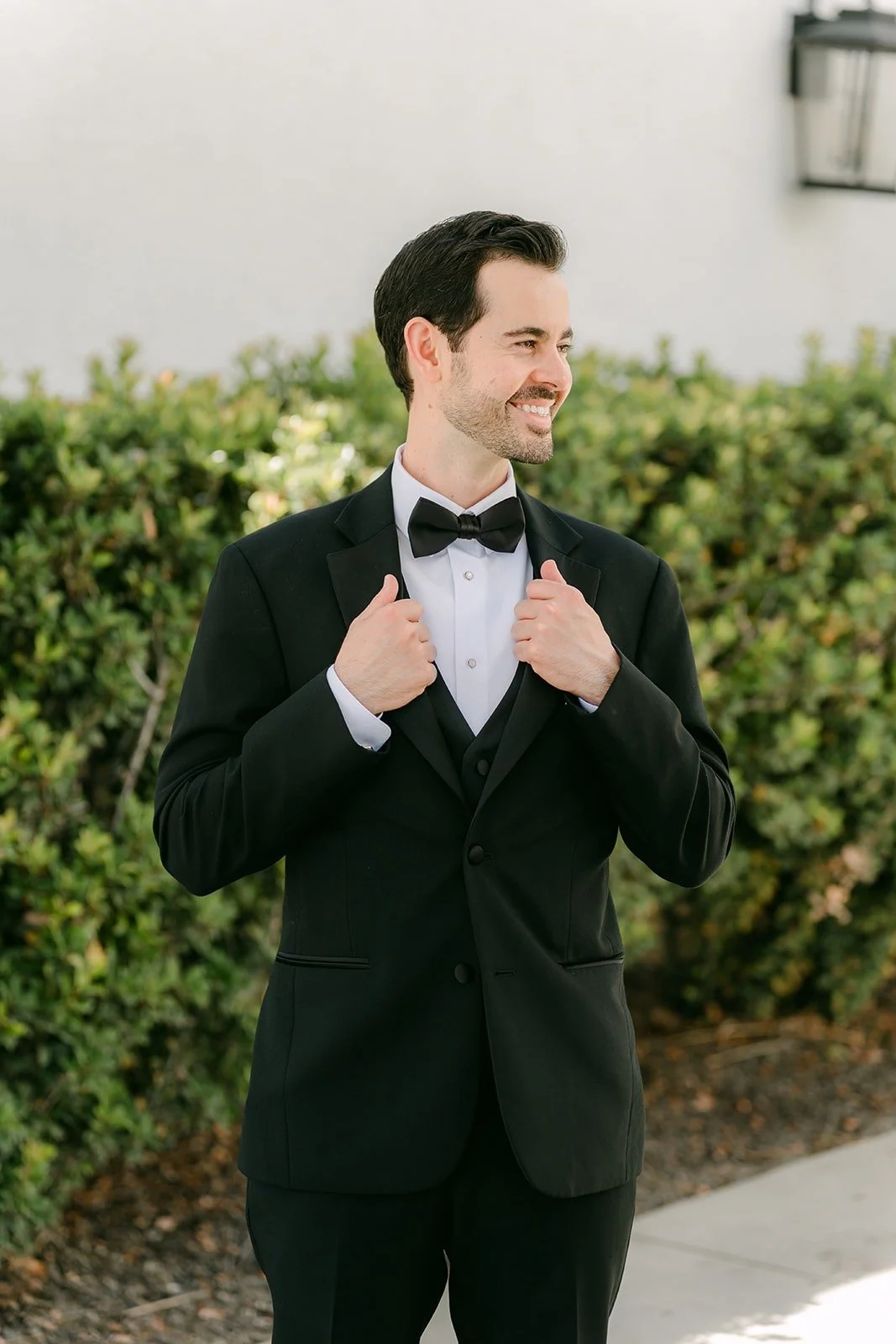 Kevin adjusting his lapels in front of a green hedge at Sterling Hills