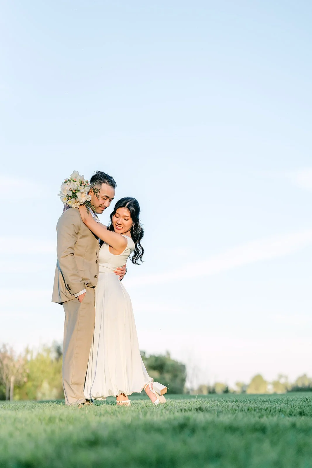 Vincent holds Kim close on the meadow with clear sky behind them.