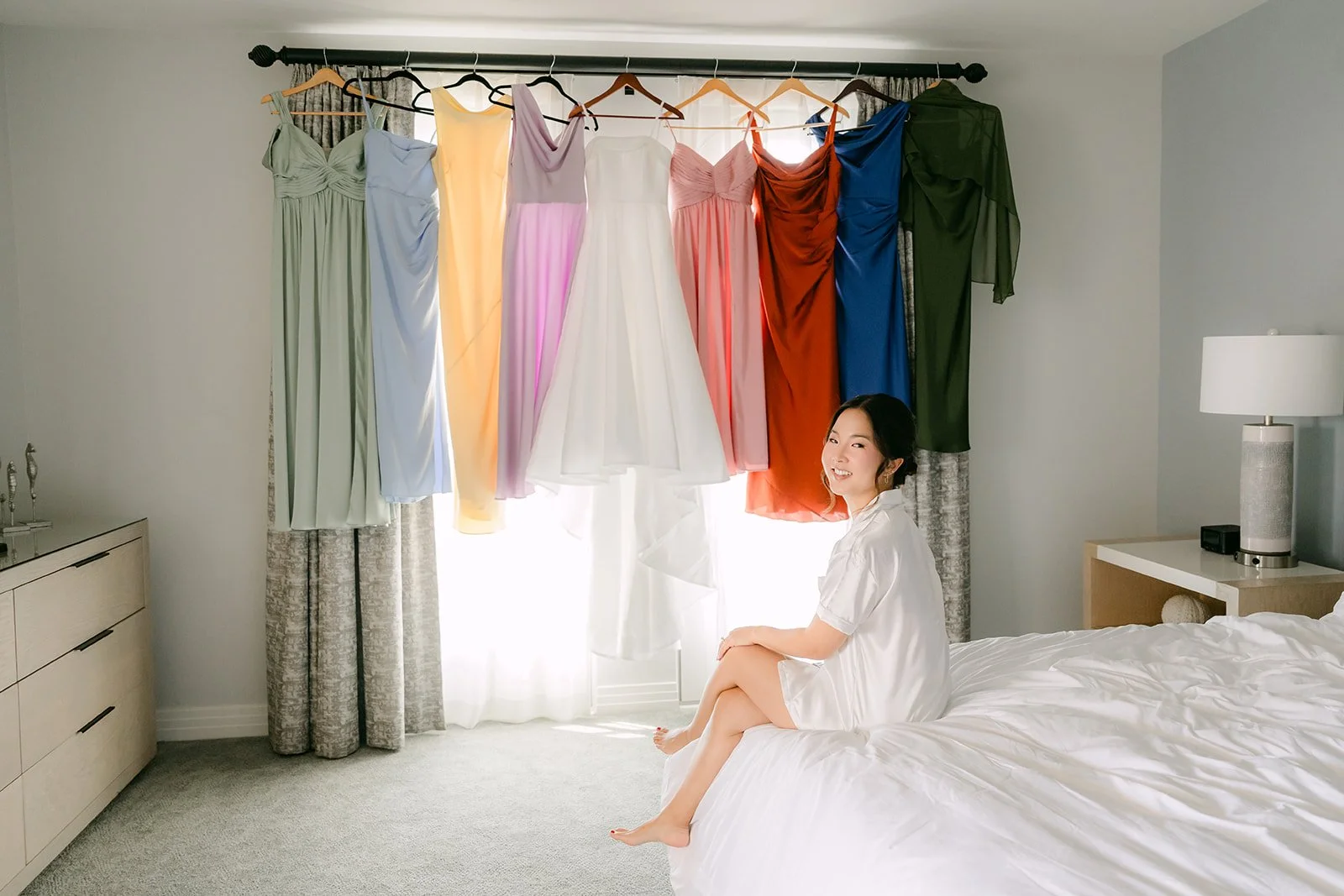 Rainbow of mismatched bridesmaid dresses hung above the bed