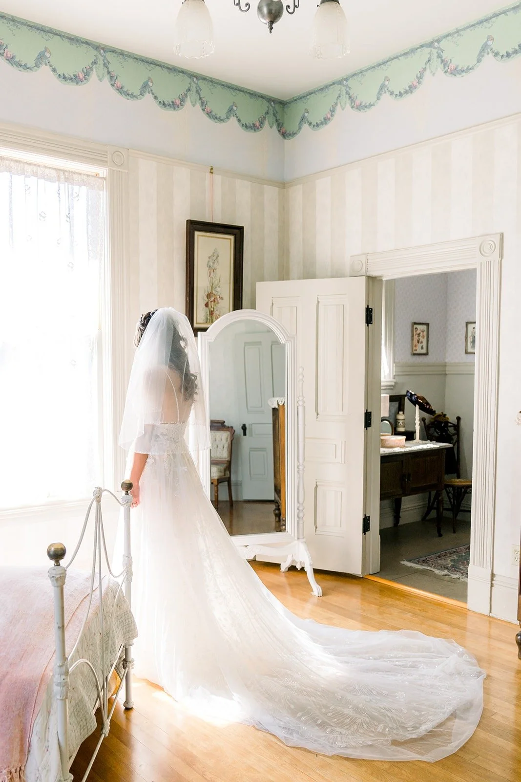Ariel in her gown and cathedral veil by the window