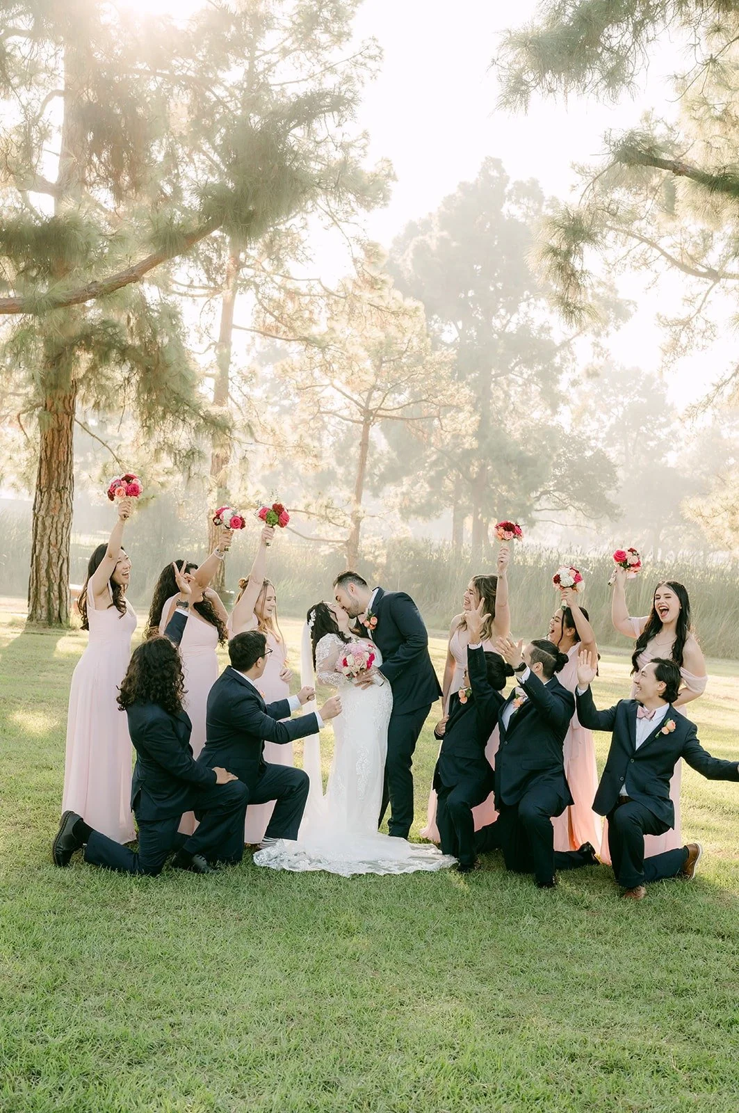 Wedding party kneeling around Amy and James, bouquets in the air