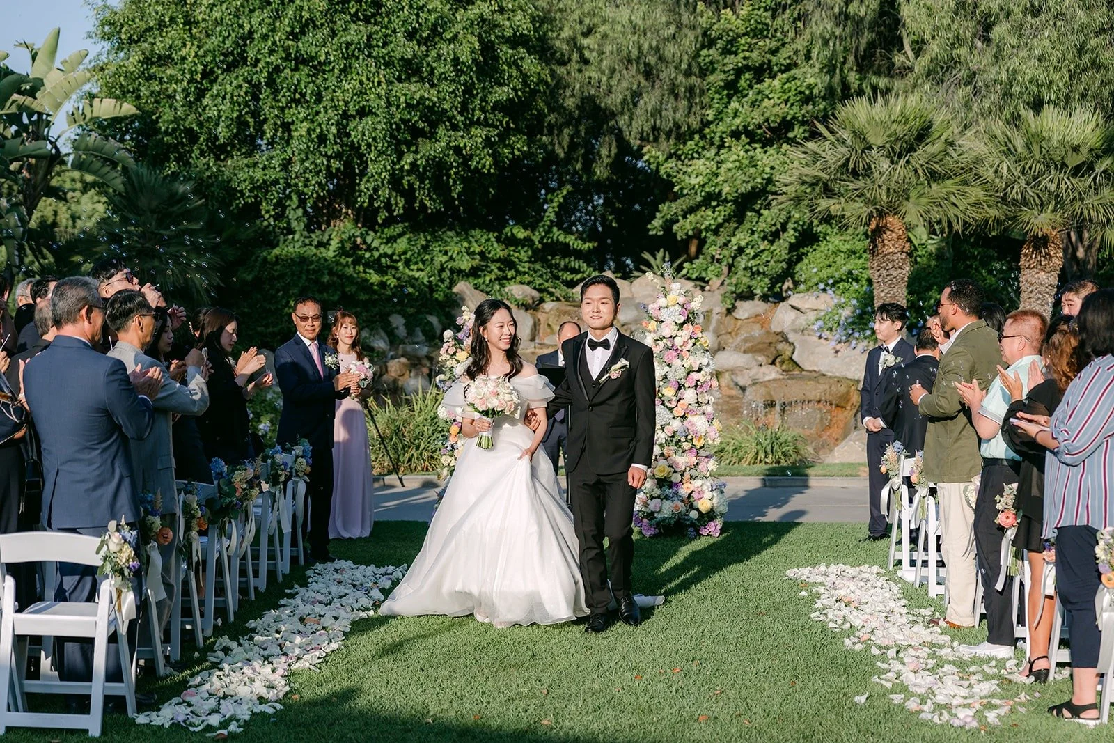 Jeannie and Eunsang at the end of the aisle with guests on both sides, photographed by One and Only Production