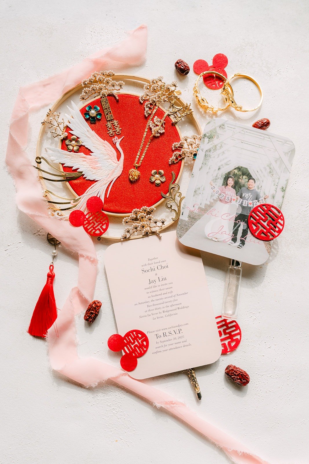 Flat lay of a red and gold wedding fan, invitation, engagement photo and red double happiness details