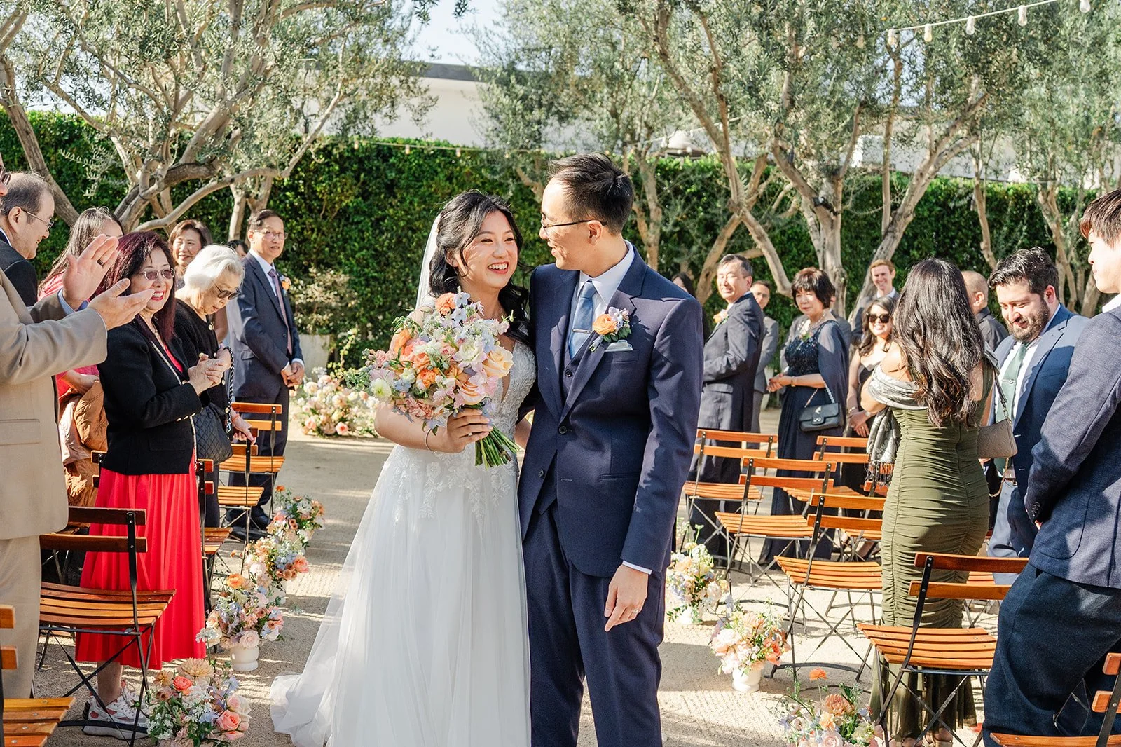 Newlyweds walking back up the aisle as guests cheer, photographed by One and Only Production