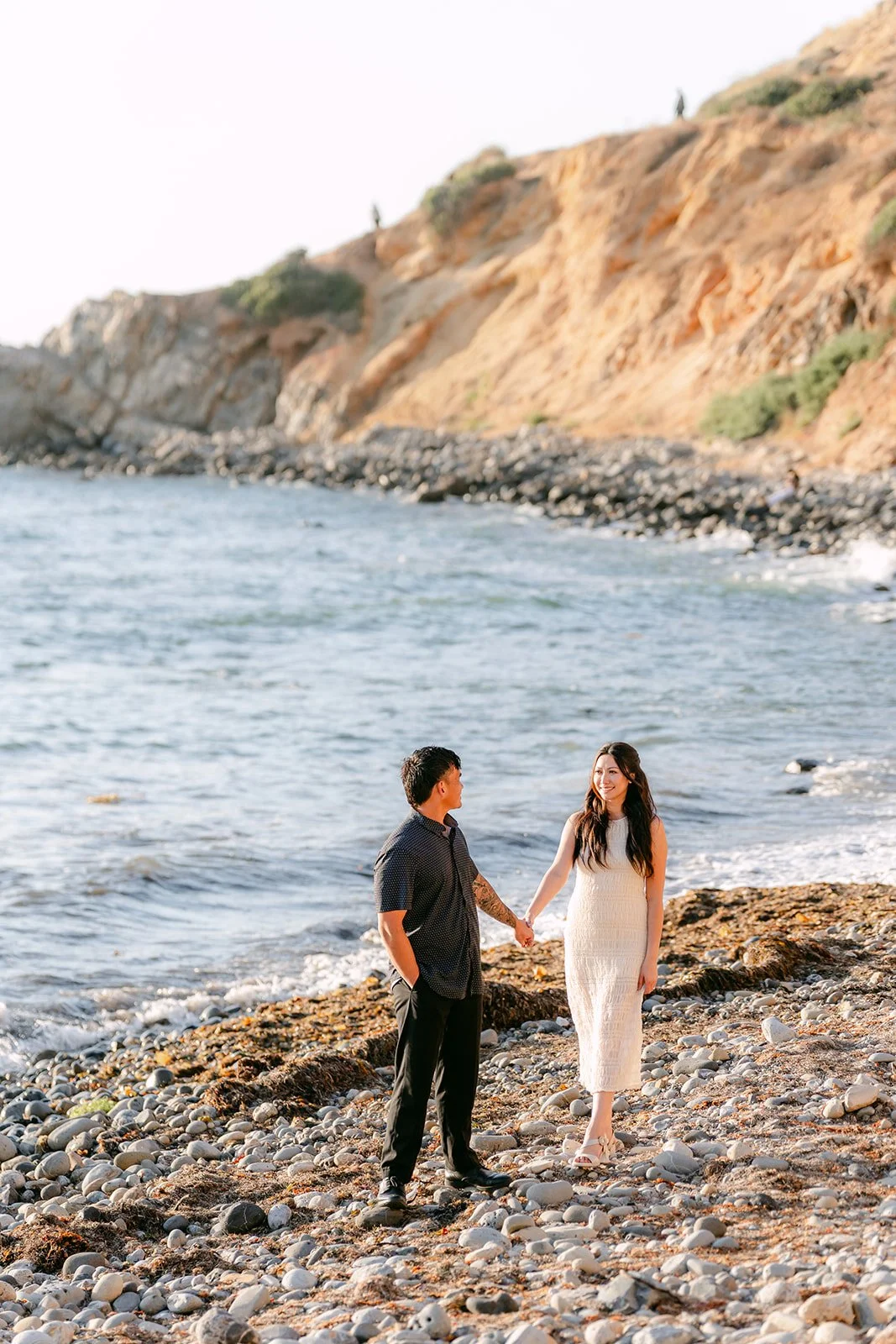 Victoria and Andrew hold hands on the pebble beach beneath the bluffs.