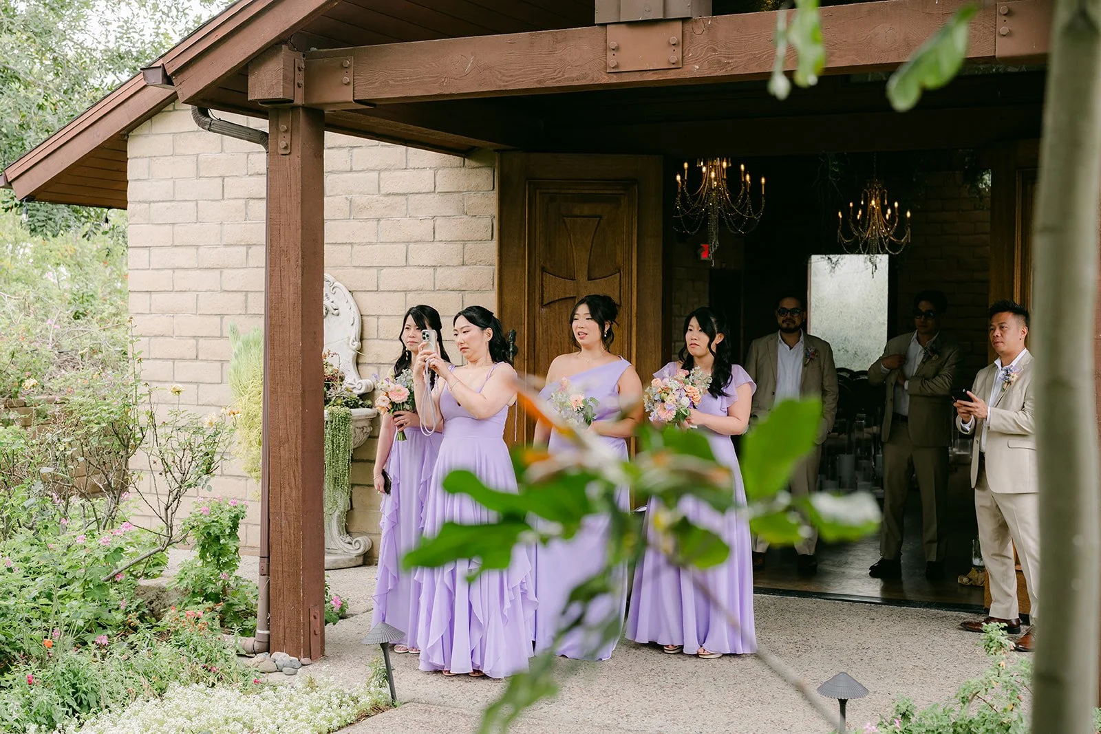 Bridesmaids in lavender peeking from the cottage porch during the first look