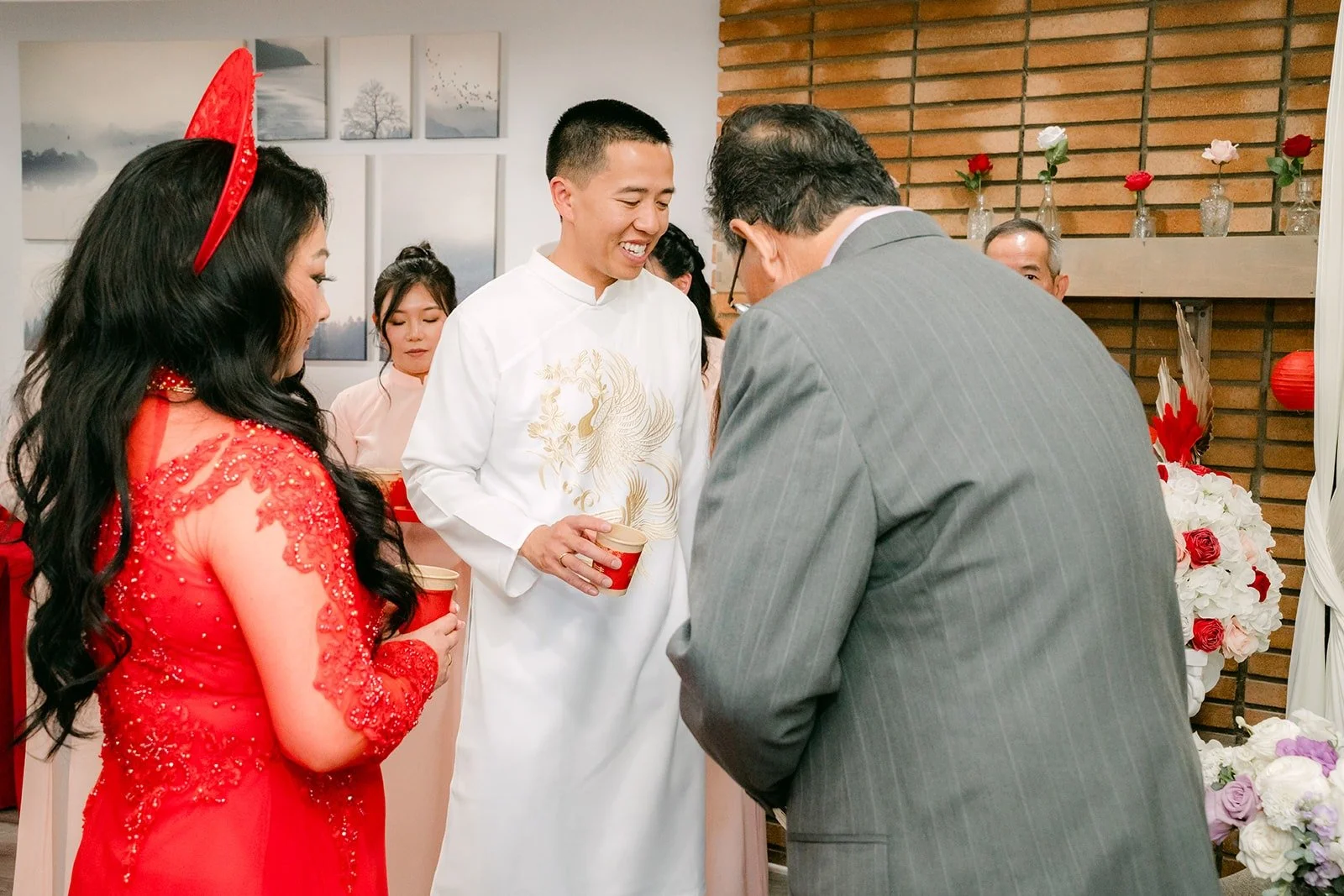 Jennifer and Kevin serve tea to a family member in front of the double happiness backdrop