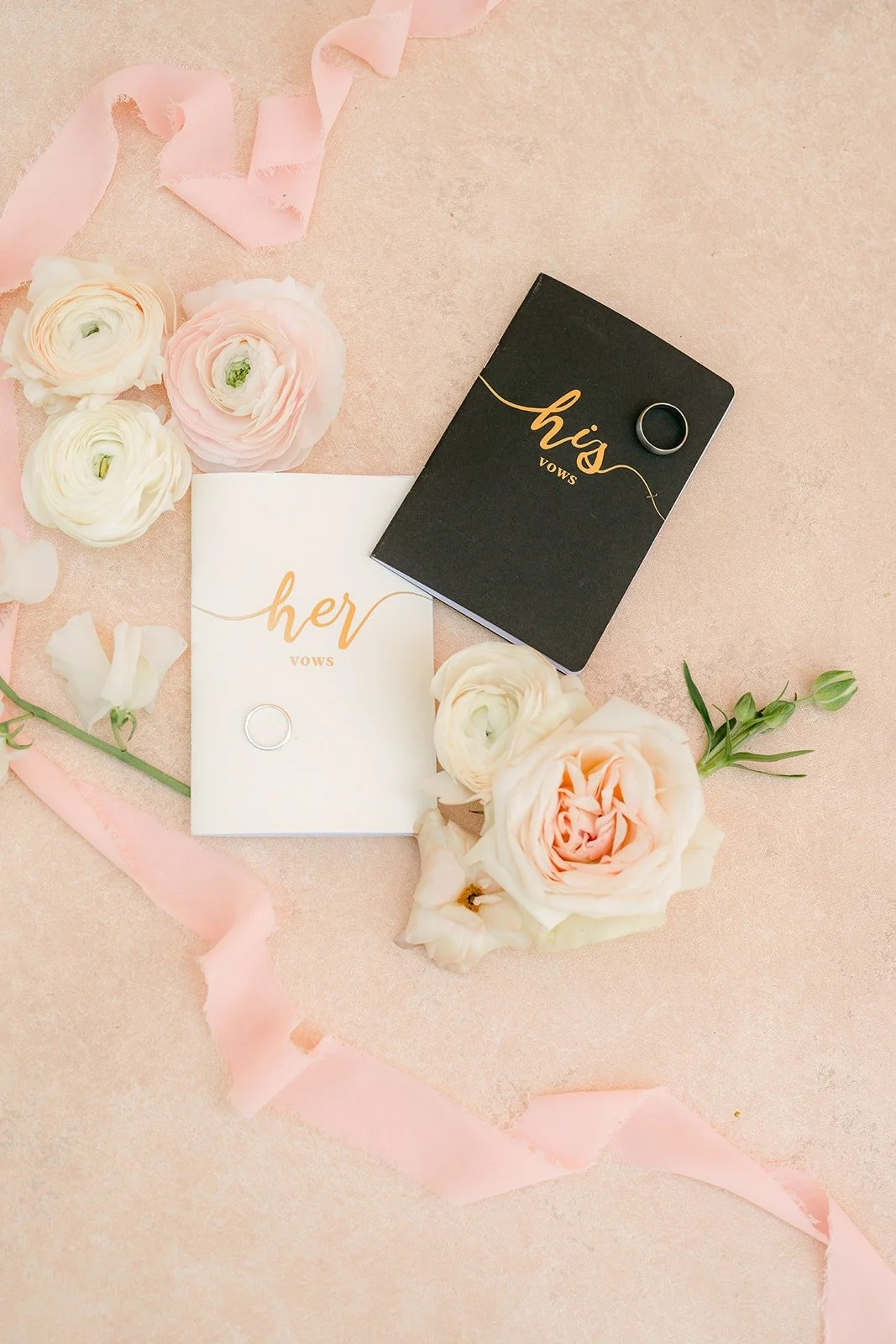 A black vow book with gold lettering among ivory and blush roses