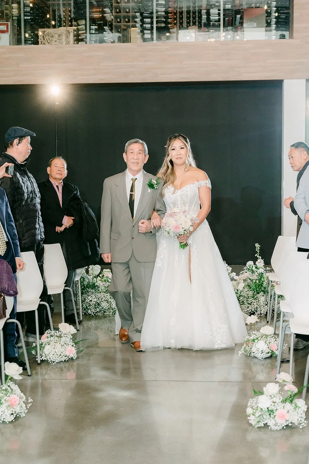Bride and her father coming down the aisle past white chairs and florals