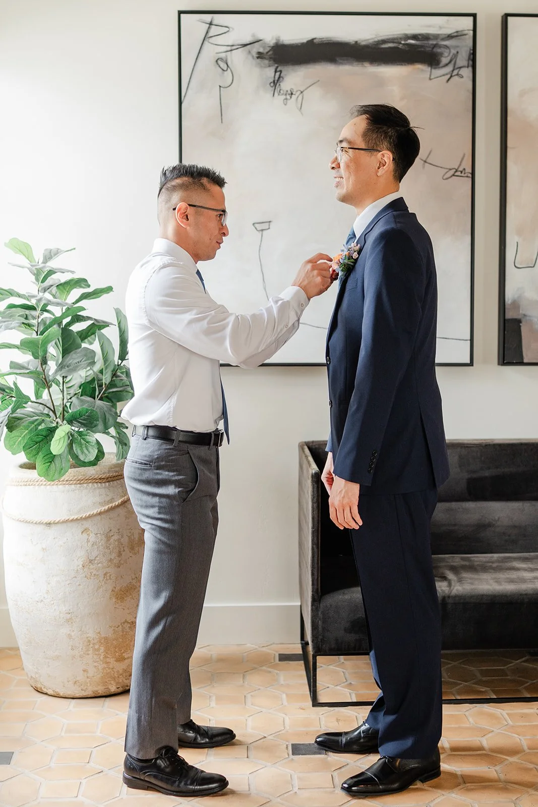 Groomsman pinning a boutonniere on Lawrence's navy suit
