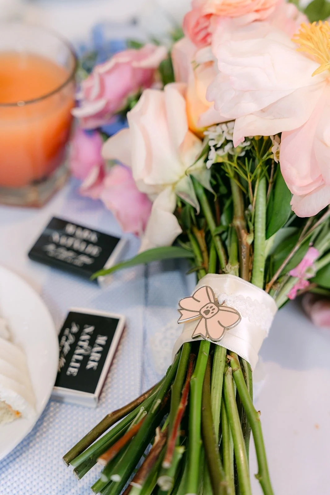 A bridesmaid's bouquet resting by a matchbook favor and a cocktail, photographed by One and Only Production