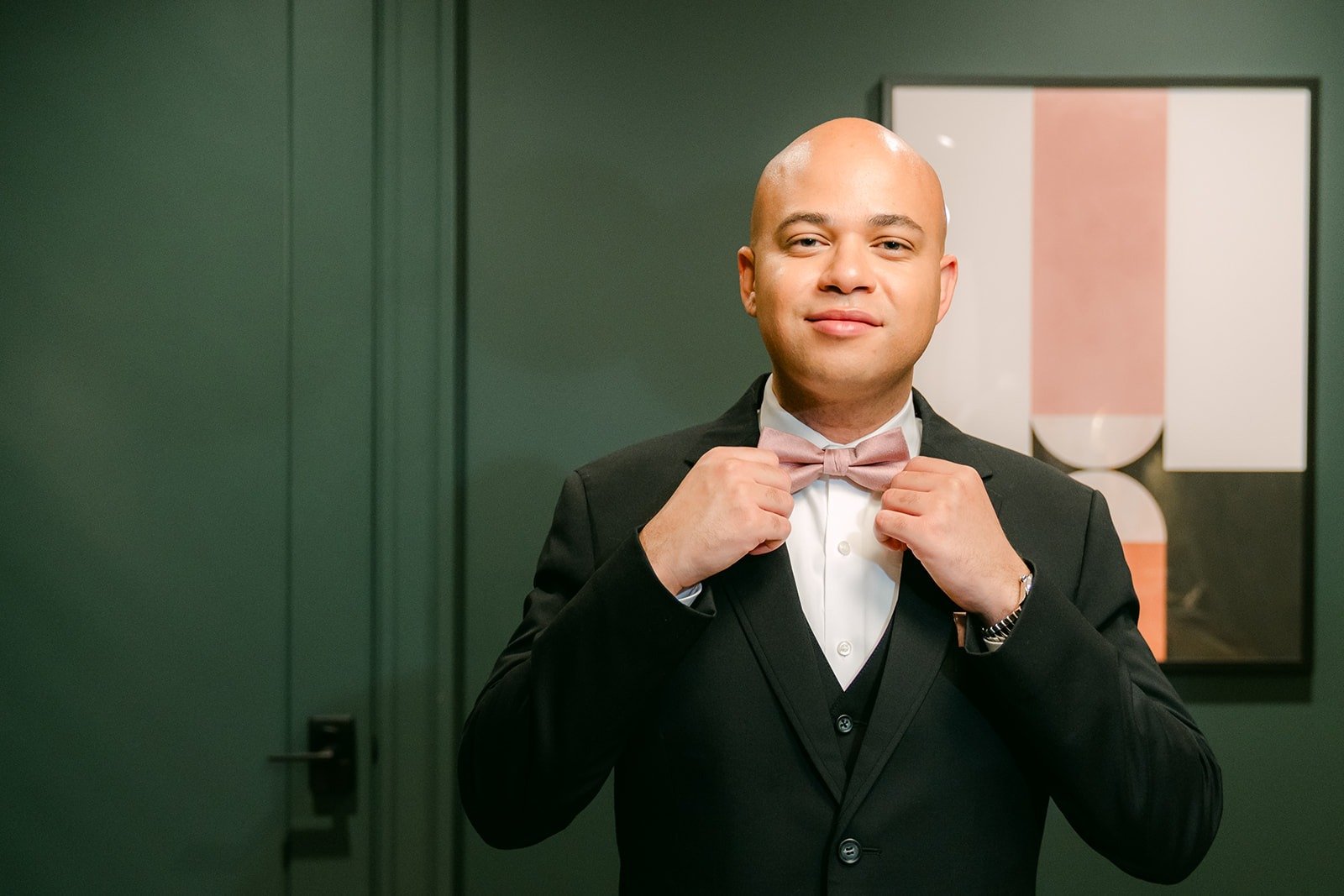 Brandon adjusts his bow tie in the dark green groom's suite