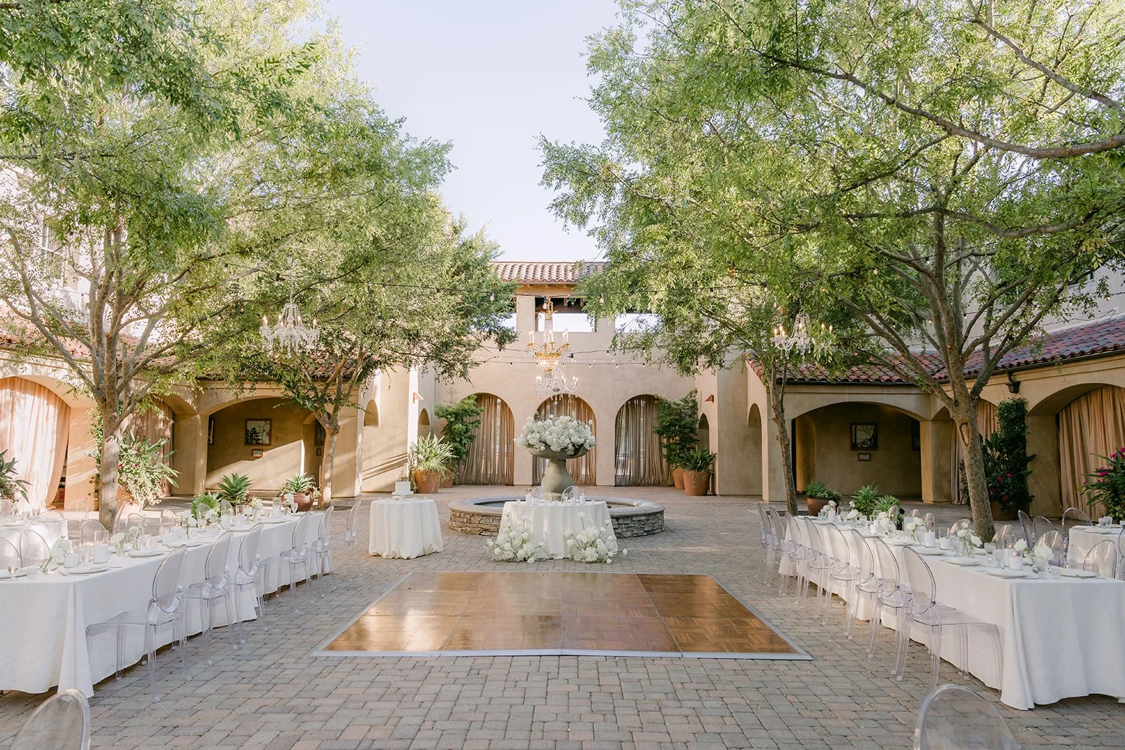 Wide view of the courtyard reception with a wood dance floor and ivory tables