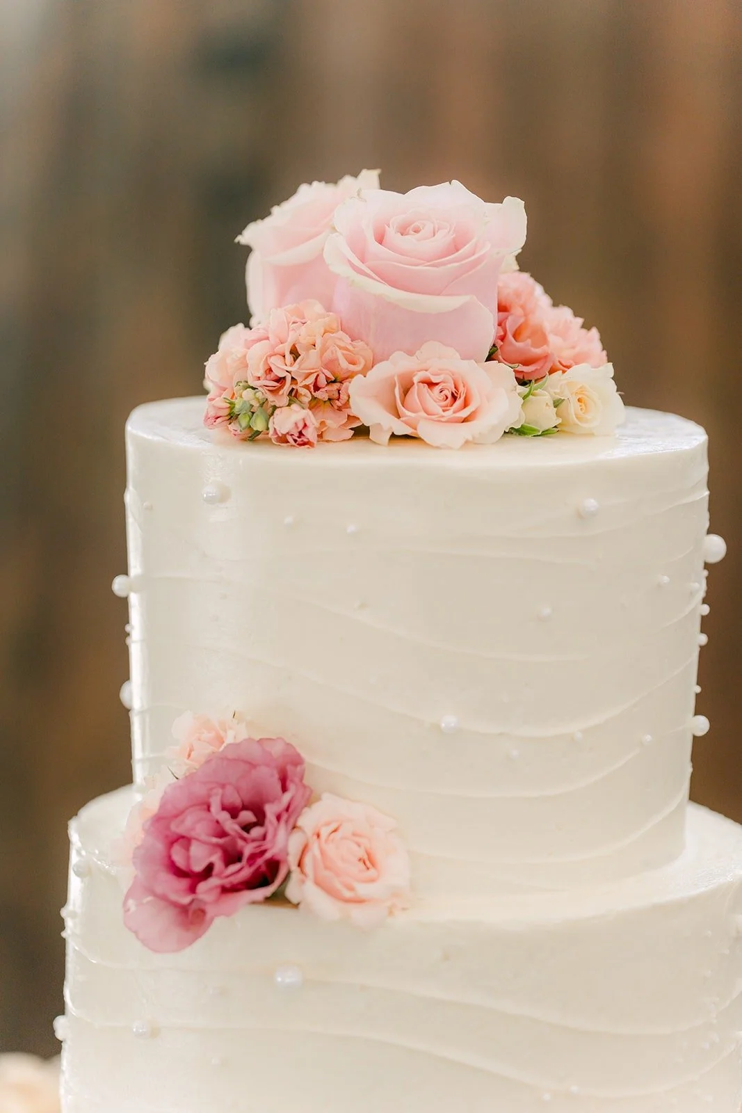 The white tiered wedding cake topped with pink roses