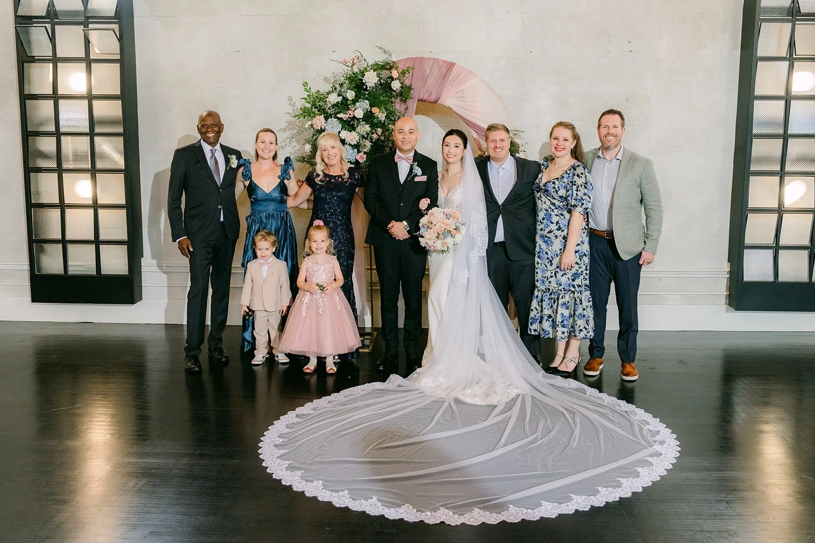 A large group of family and friends gathered around Elisa and Brandon at the arch