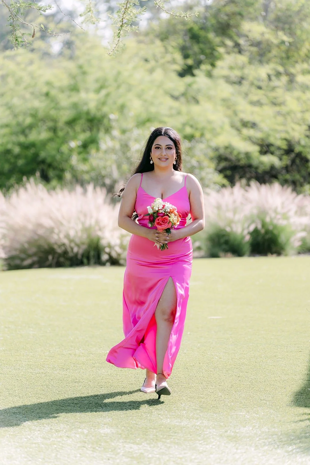 A bridesmaid in pink walking down the aisle with her bouquet