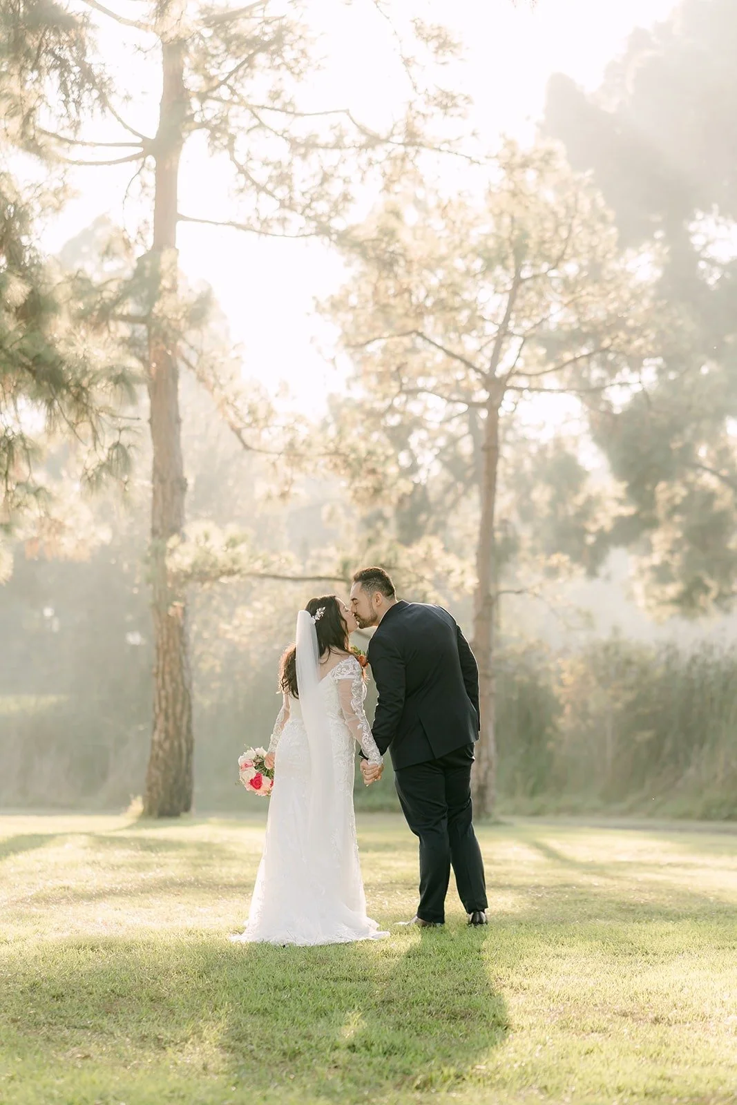 Amy and James small in the frame under tall trees and morning sun