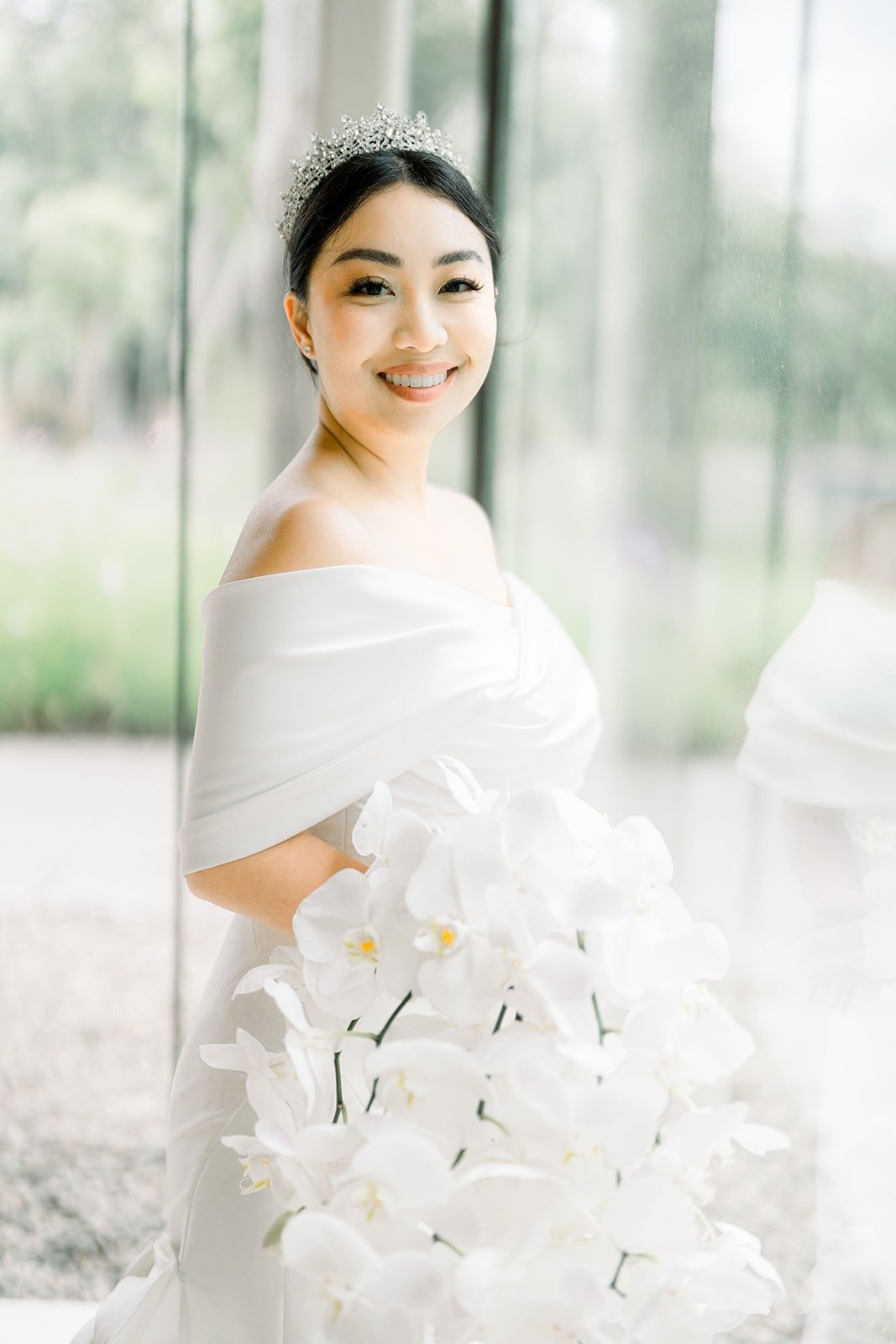 Jacinda in an off the shoulder gown and tiara holding white orchids
