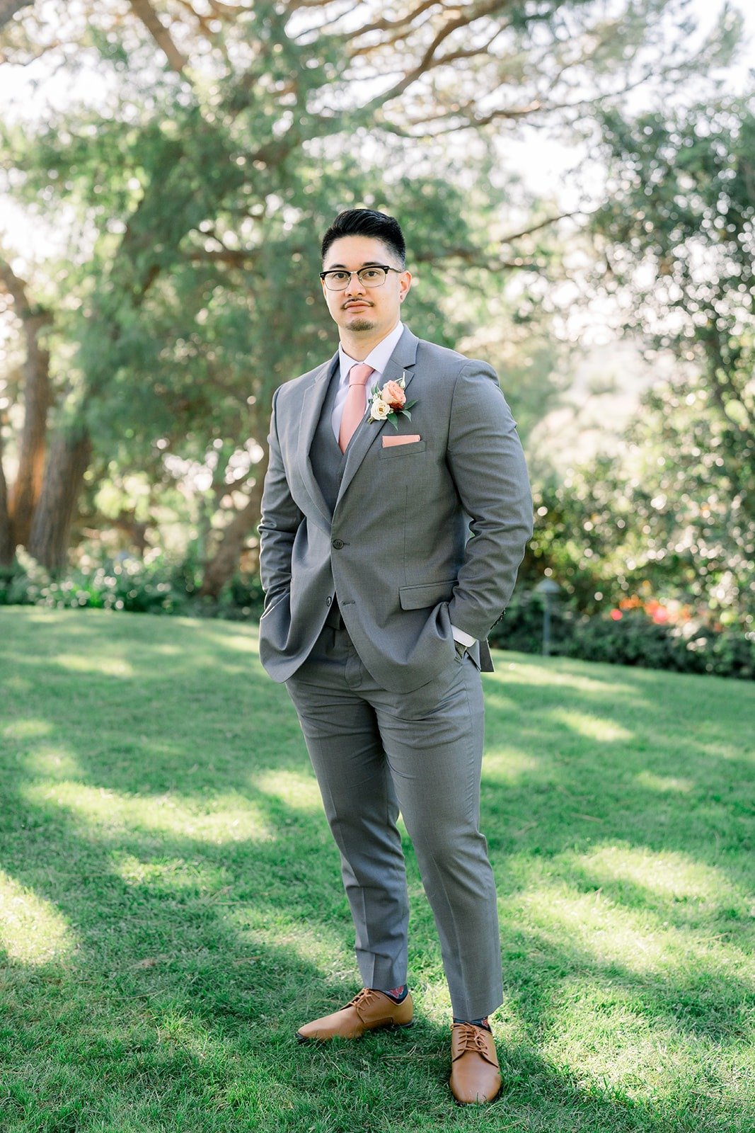Mikey in a grey three piece suit and blush pink tie on the lawn