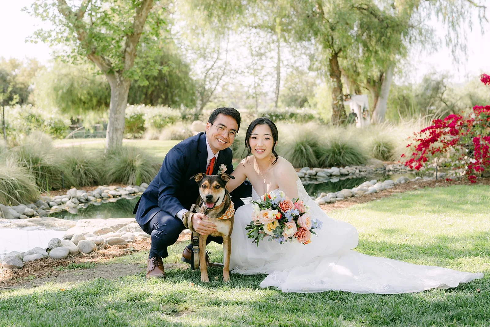 Yishan and Jonathan sitting on the grass by the water with their dog