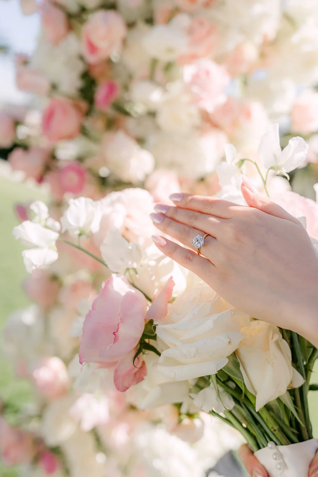 Close-up of the bride's ring and hand against blush roses