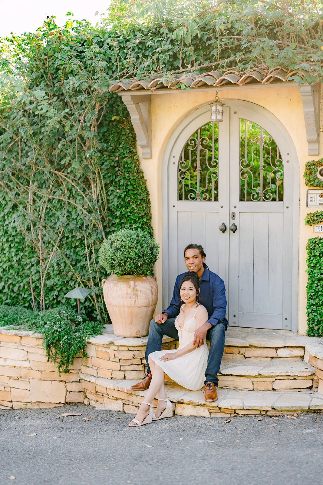 Amy and Michael sitting on stone steps in front of a white arched garden door.