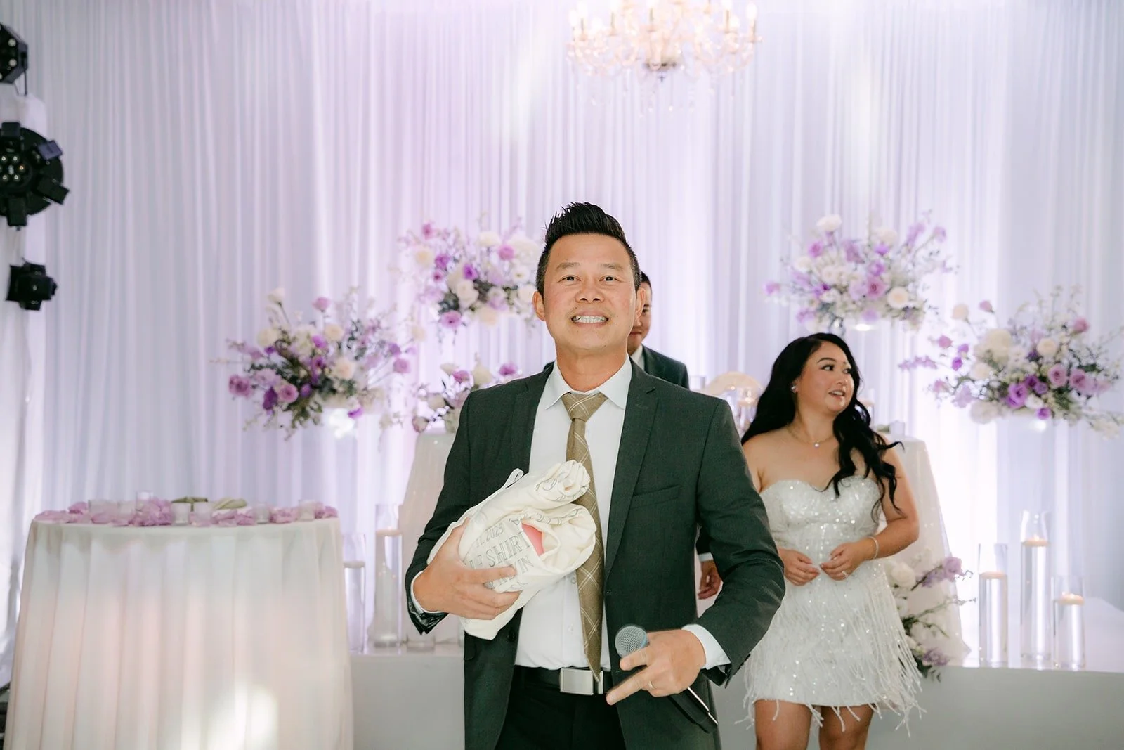 Kevin holds up a t shirt as Jennifer stands by in her white party dress