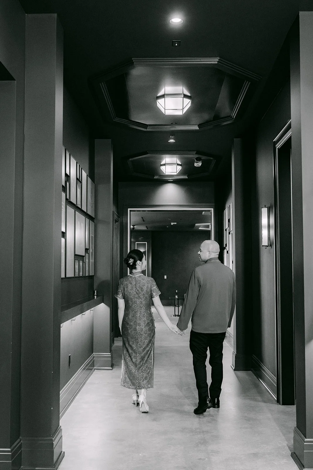 Elisa and Brandon walk hand in hand down a dark hallway