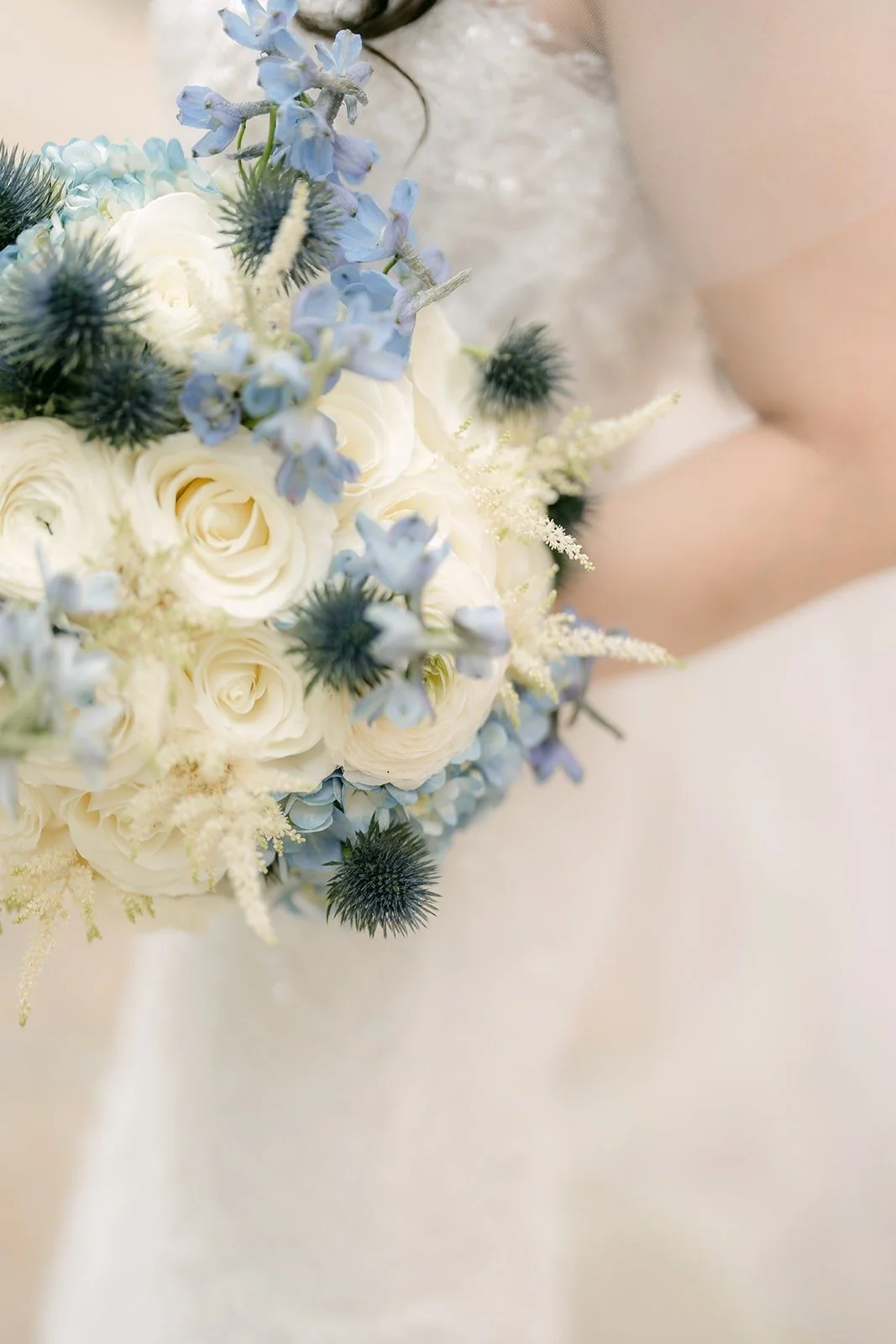 Close up of Emily's bouquet with white roses and blue thistle