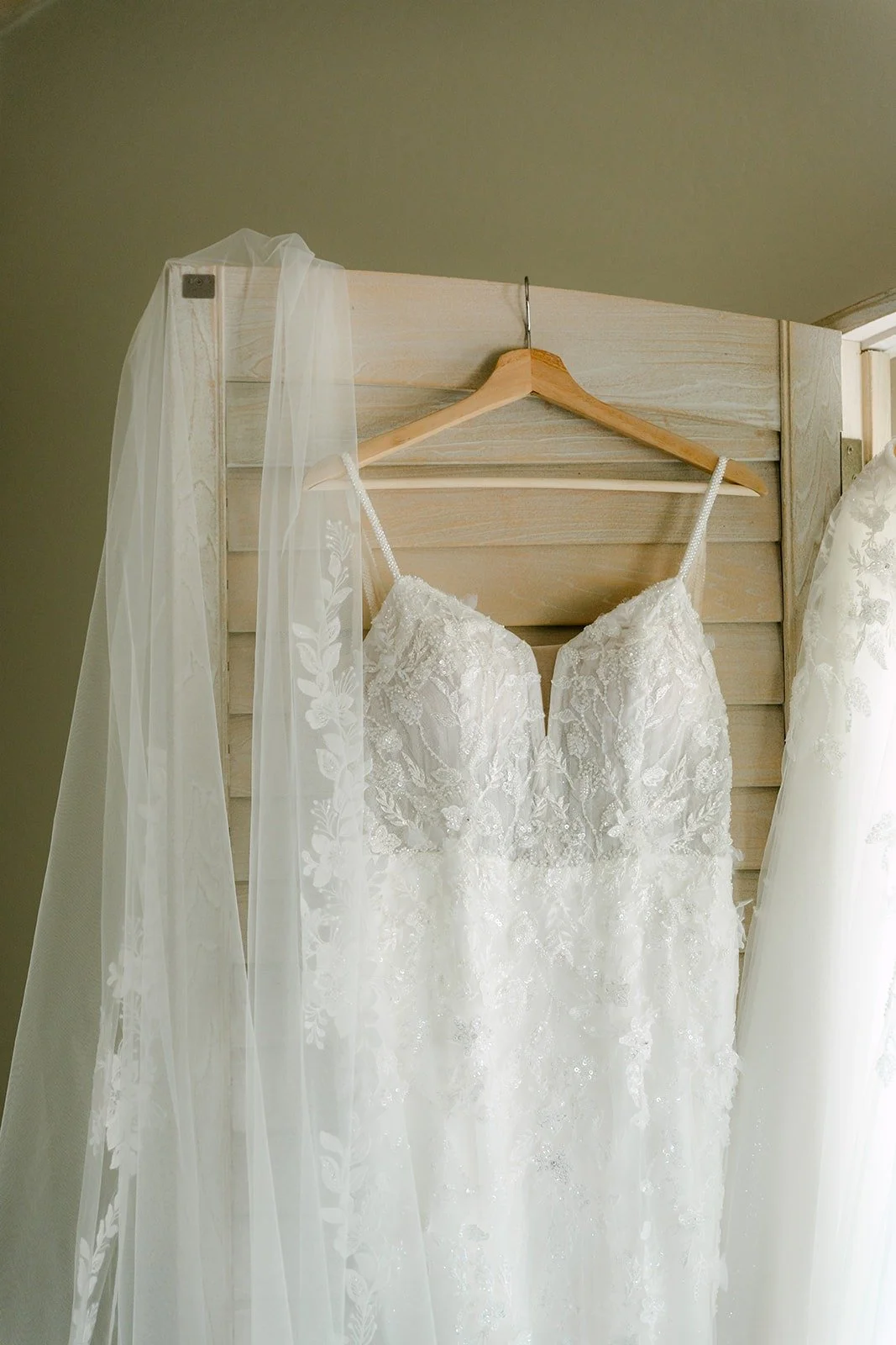 Joanne's wedding gown and veil hanging on a wooden hanger