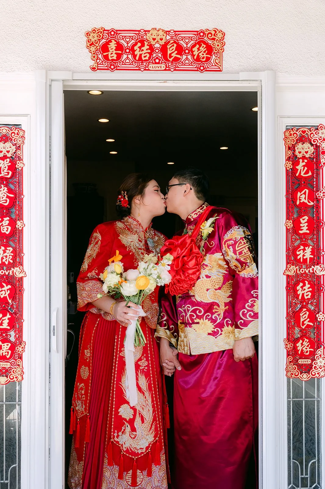 The bride and groom sharing a kiss in the doorway between red couplets.