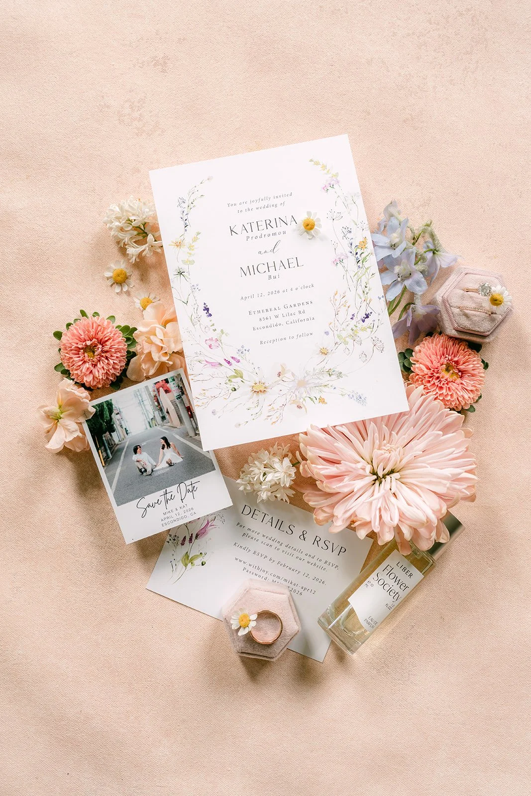 Wedding flat lay with a floral invitation suite, perfume and pastel flowers on blush linen
