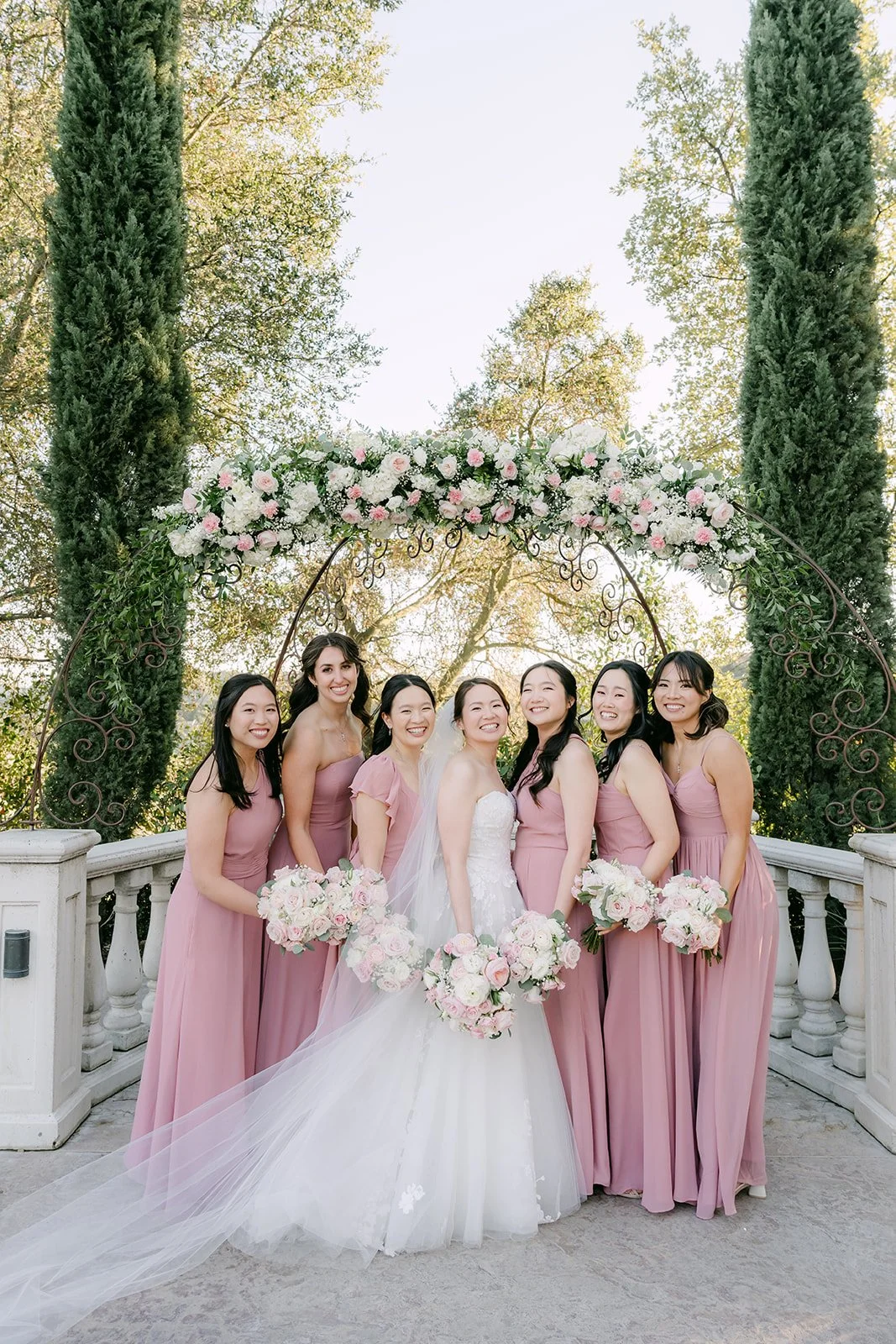 Bride and bridesmaids in dusty rose under the floral ceremony arch