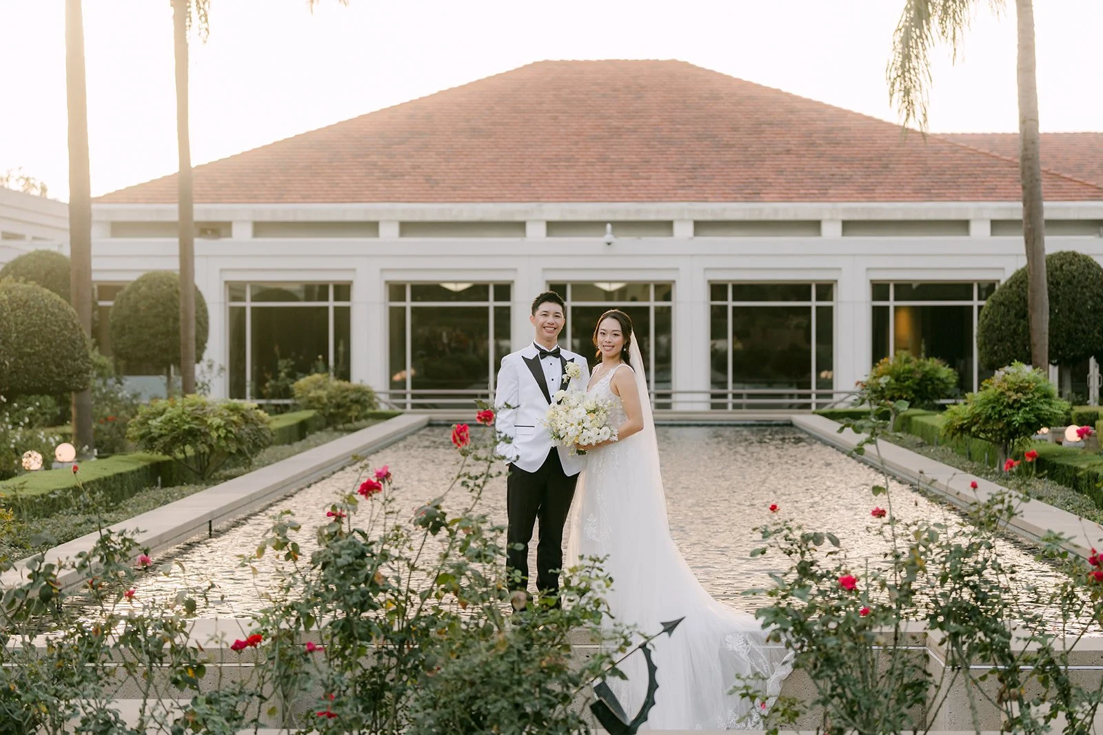Jenny and Ryan in the rose garden in front of a red tile roof.