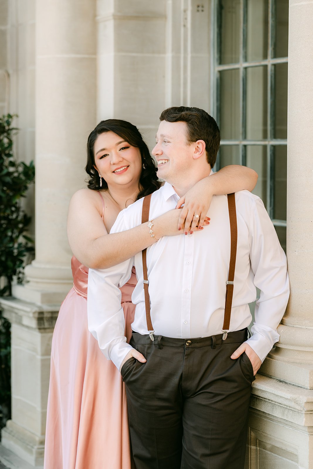 Saira wraps her arms around Matthew beside the window frame.